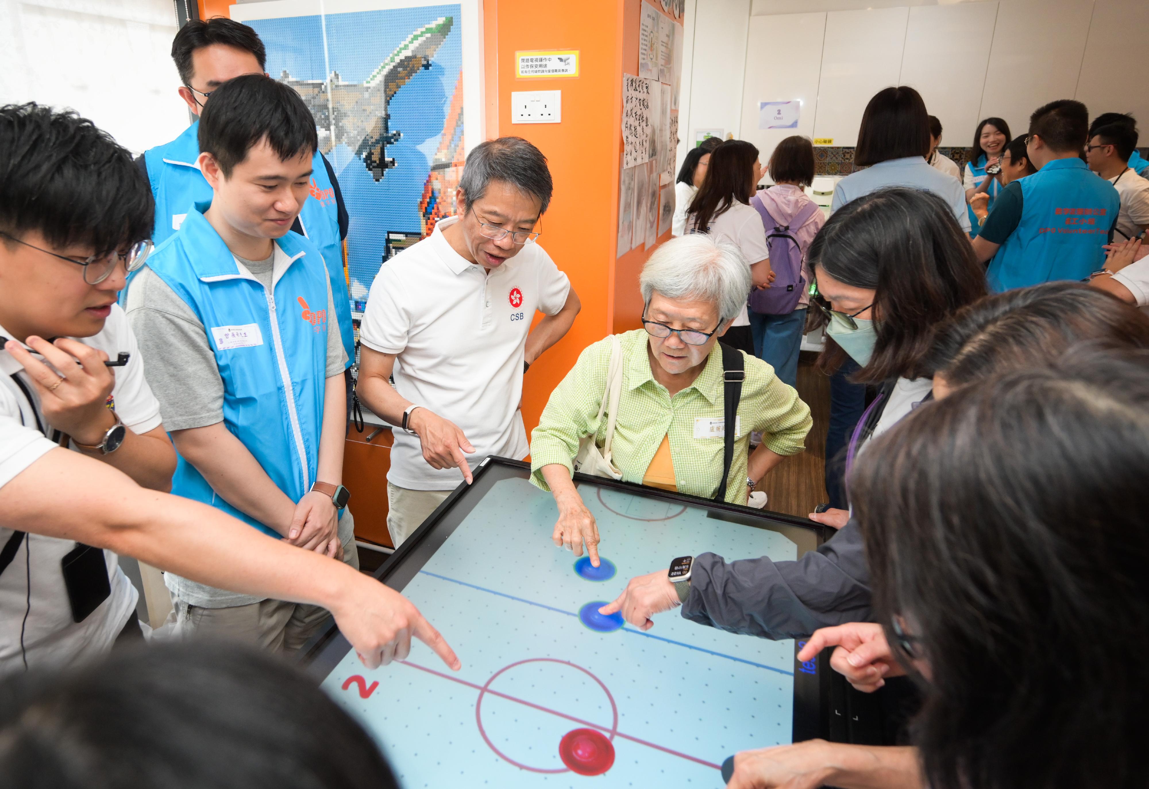The Civil Service Bureau (CSB) Volunteer Team and the Digital Policy Office Volunteer Team today (May 17) visited the Hong Kong Sheng Kung Hui (HKSKH) Lok Man Alice Kwok Integrated Service Centre in To Kwa Wan to carry out volunteer service under the "Smart Silver" Digital Inclusion Programme for Elders. They assisted the elderly to learn how to use smartphones and mobile applications and had fun from gerontechnology through interactive activities and integration of technology into daily lives. Photo shows the Permanent Secretary for the Civil Service, Mr Clement Leung (third left), and civil service volunteers playing games for cognitive training with the elderly to help enhance the elderly's responsive abilities.