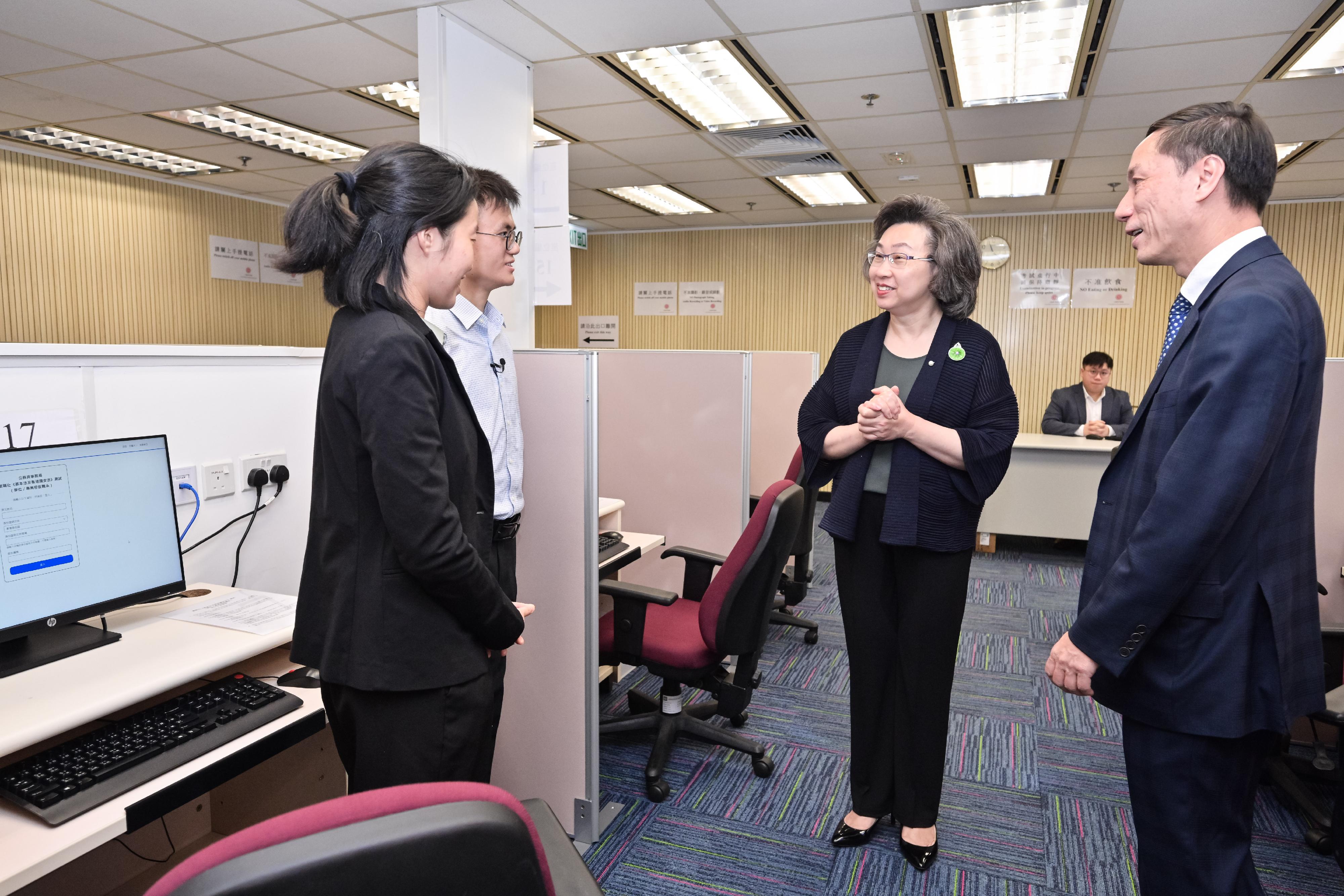 公務員事務局推出數碼化《基本法及香港國安法》測試（學位／專業程度職系）（數碼化測試），有意報考人士可於明日（五月二十一日）上午九時起透過公務員事務局網頁網上系統，預約五月二十三日或之後的考試時段。圖示公務員事務局局長楊何蓓茵（右二）在數碼化測試推出前，到一般職系處招聘中心視察在該處進行數碼化測試的安排和流程。兩名參與行政主任職系職前實習計劃的同學向局長分享他們參與系統模擬測試的經驗。旁為公務員事務局一般職系處長陳信禧（右一）。