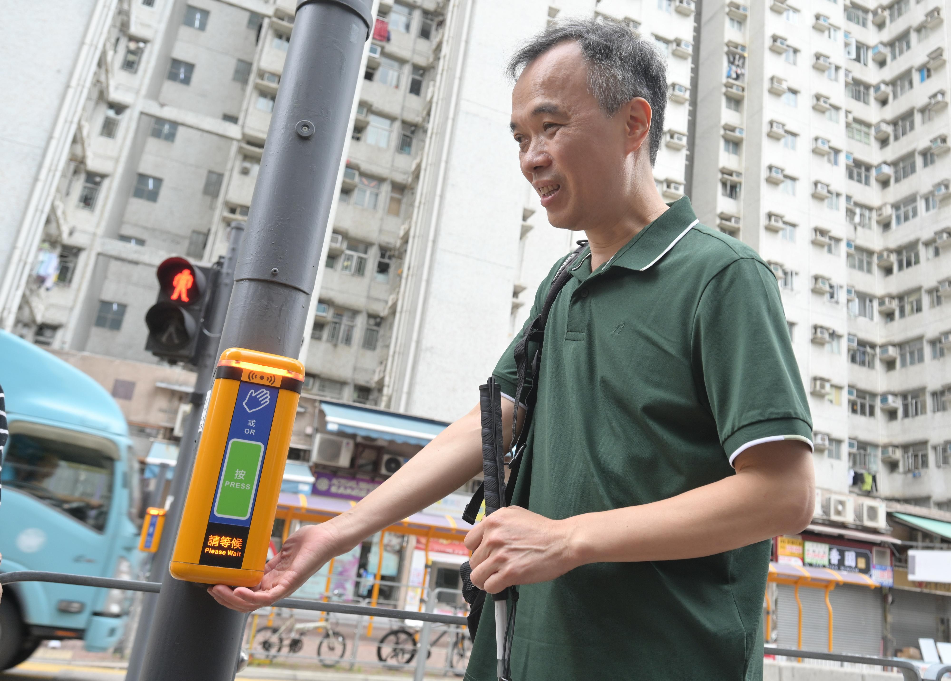The Transport Department today (May 20) announced the territory-wide gradual renewal of electronic audible traffic signals (eATS) at signalised crossings. People-oriented new features have been incorporated to provide convenience for visually impaired persons and other members of the public. Photo shows a visually impaired person pressing the pedestrian push button at the bottom of the new eATS before crossing the road under the green signal.