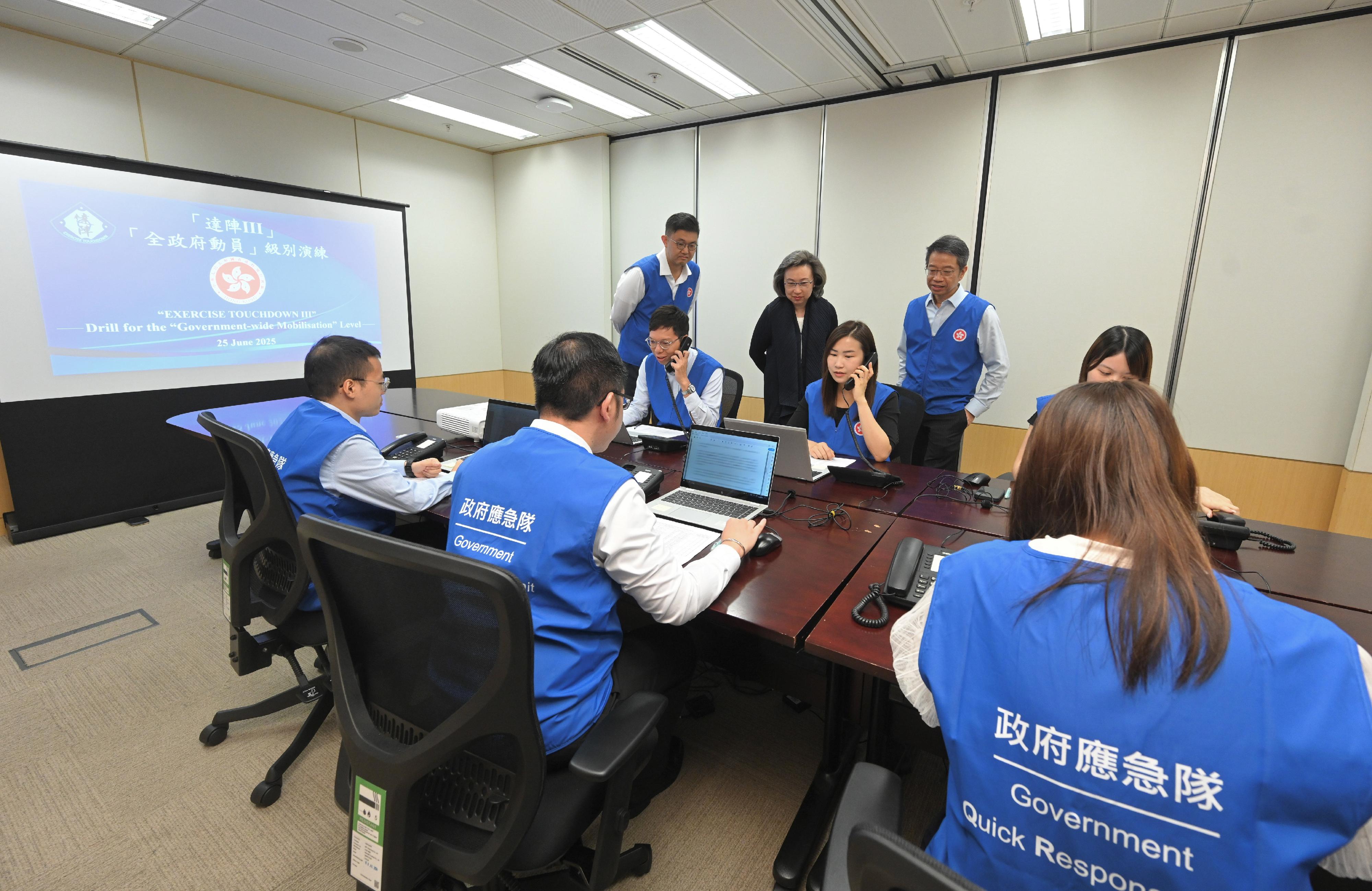 公務員事務局今日（六月二十五日）舉行代號為「達陣III」的「全政府動員」級別桌面演練，集中測試全政府所有部門的動員效率和跨部門聯絡通訊機制的效能，藉此讓各部門進一步熟習動員機制的運作，鞏固提升政府跨部門動員和應變能力。圖示公務員事務局局長楊何蓓茵（後排中）及公務員事務局常任秘書長梁卓文（後排右）一同聽取公務員事務局副秘書長陳元德（後排左）匯報同事與不同部門的溝通情況。