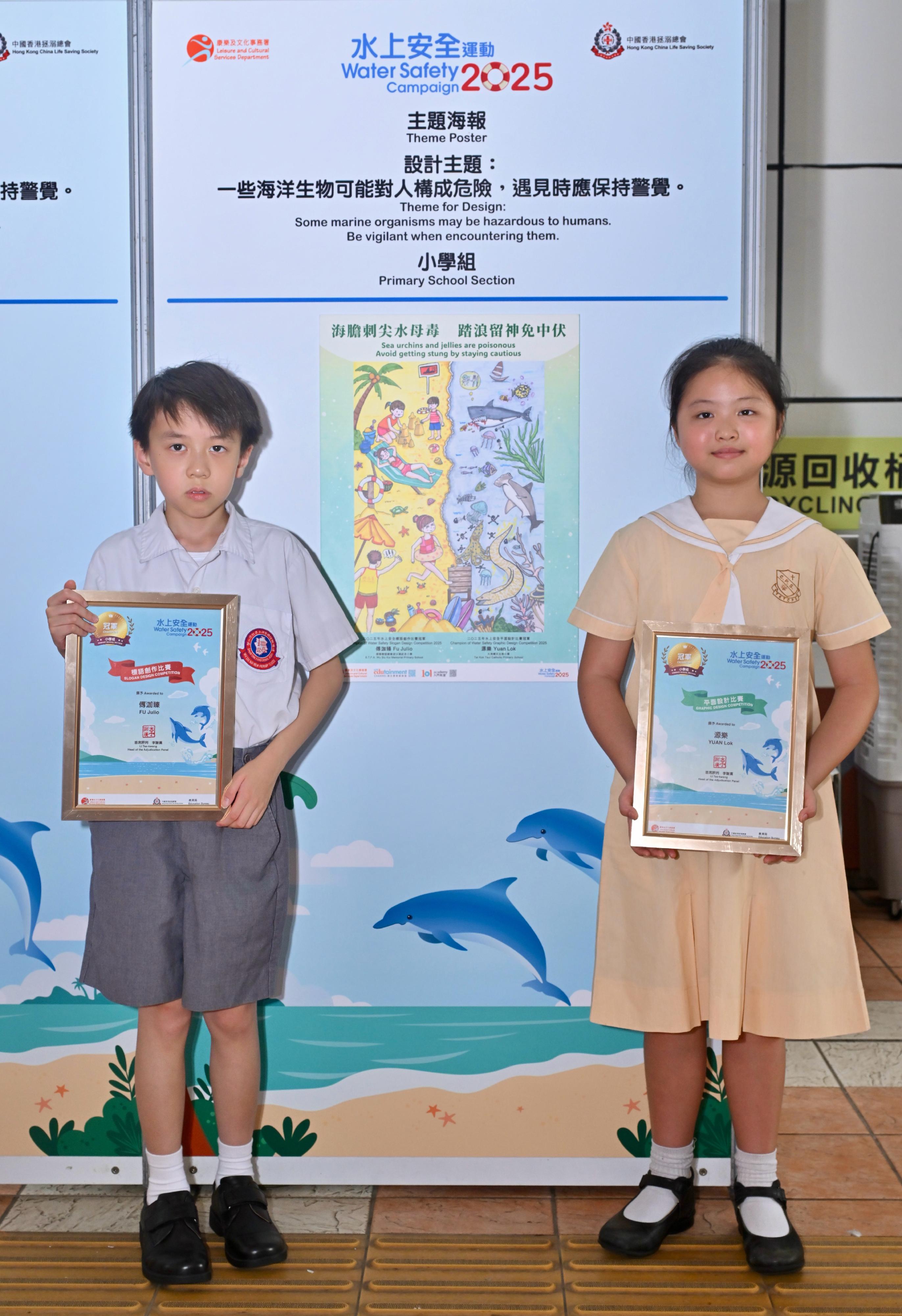 A prize presentation ceremony for the Water Safety Campaign 2025 slogan and graphic design competitions, jointly organised by the Leisure and Cultural Services Department and the Hong Kong China Life Saving Society, was held today (June 28). Pictured with his/her winning entry is the champion of the primary school section in the graphic design competition, Yuan Lok (right), and the champion of the primary school section in the Chinese slogan competition, Julio Fu (left).