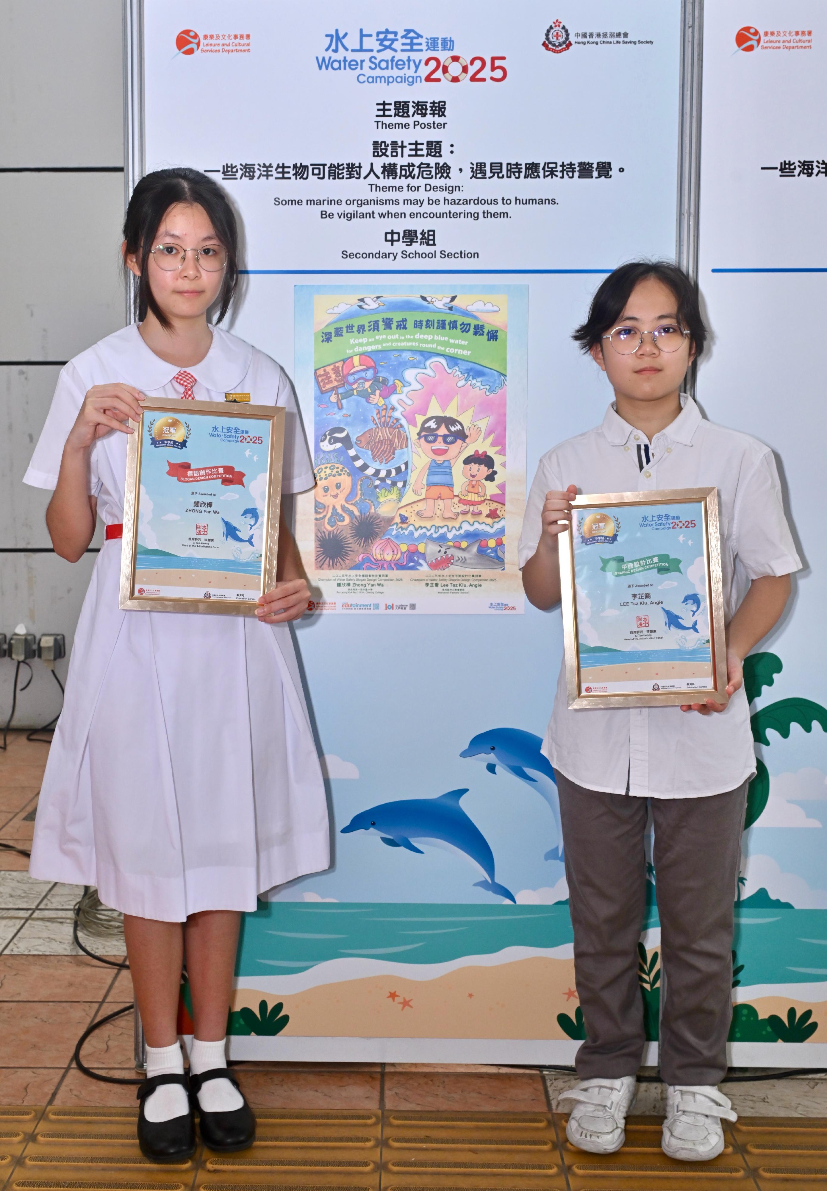 A prize presentation ceremony for the Water Safety Campaign 2025 slogan and graphic design competitions, jointly organised by the Leisure and Cultural Services Department and the Hong Kong China Life Saving Society, was held today (June 28). Pictured with his/her winning entry is the champion of the secondary school section in the graphic design competition, Angie Lee (right), and the champion of the secondary school section in the Chinese slogan competition, Zhong Yan-wa (left).