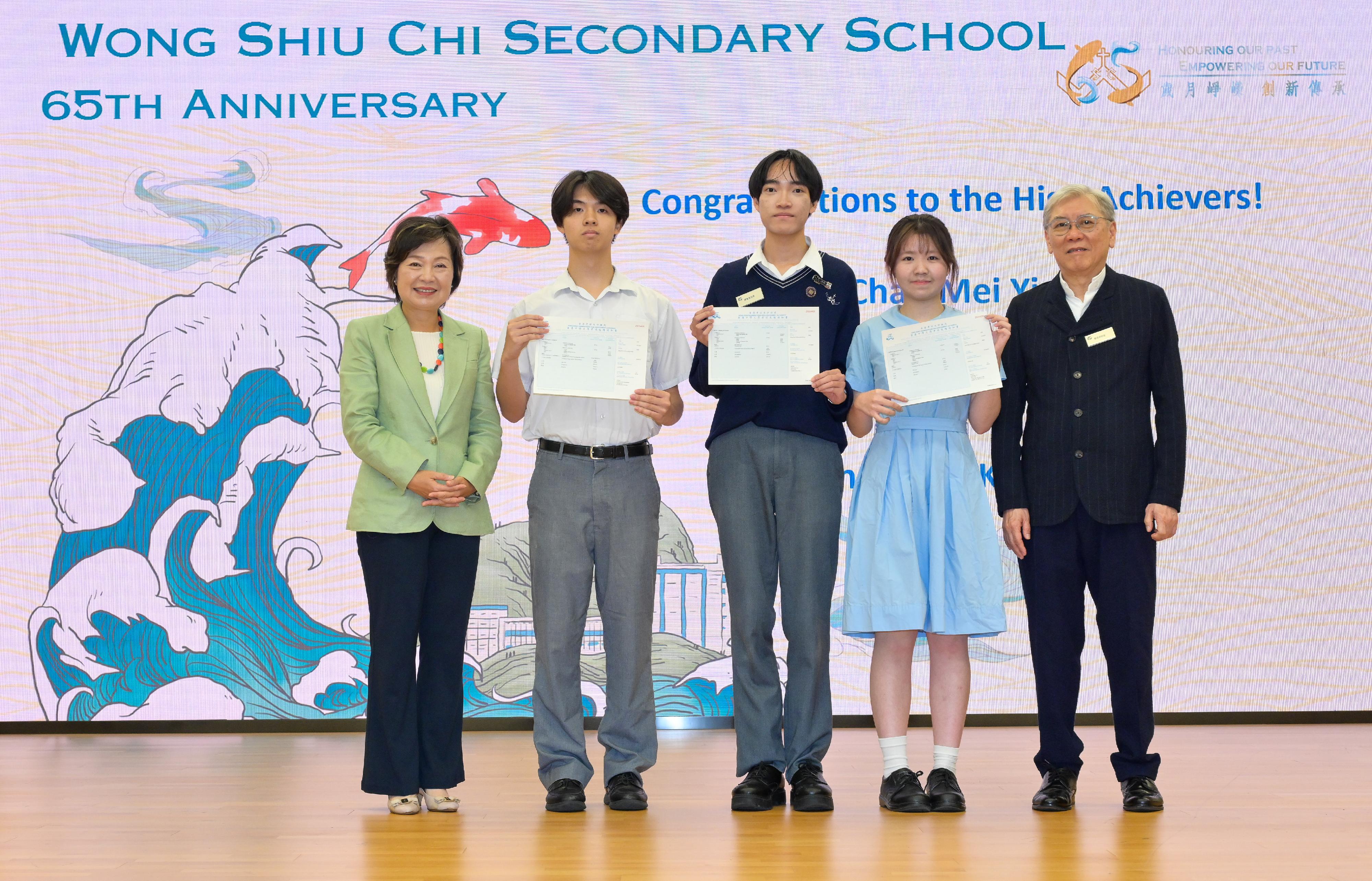 教育局局長蔡若蓮博士今日（七月十六日）到訪王肇枝中學，勉勵應屆香港中學文憑考試考生。圖示蔡若蓮博士（左一）及王肇枝中學校監鄧啟明（右一）頒發考試成績通知書予成績優異的學生。