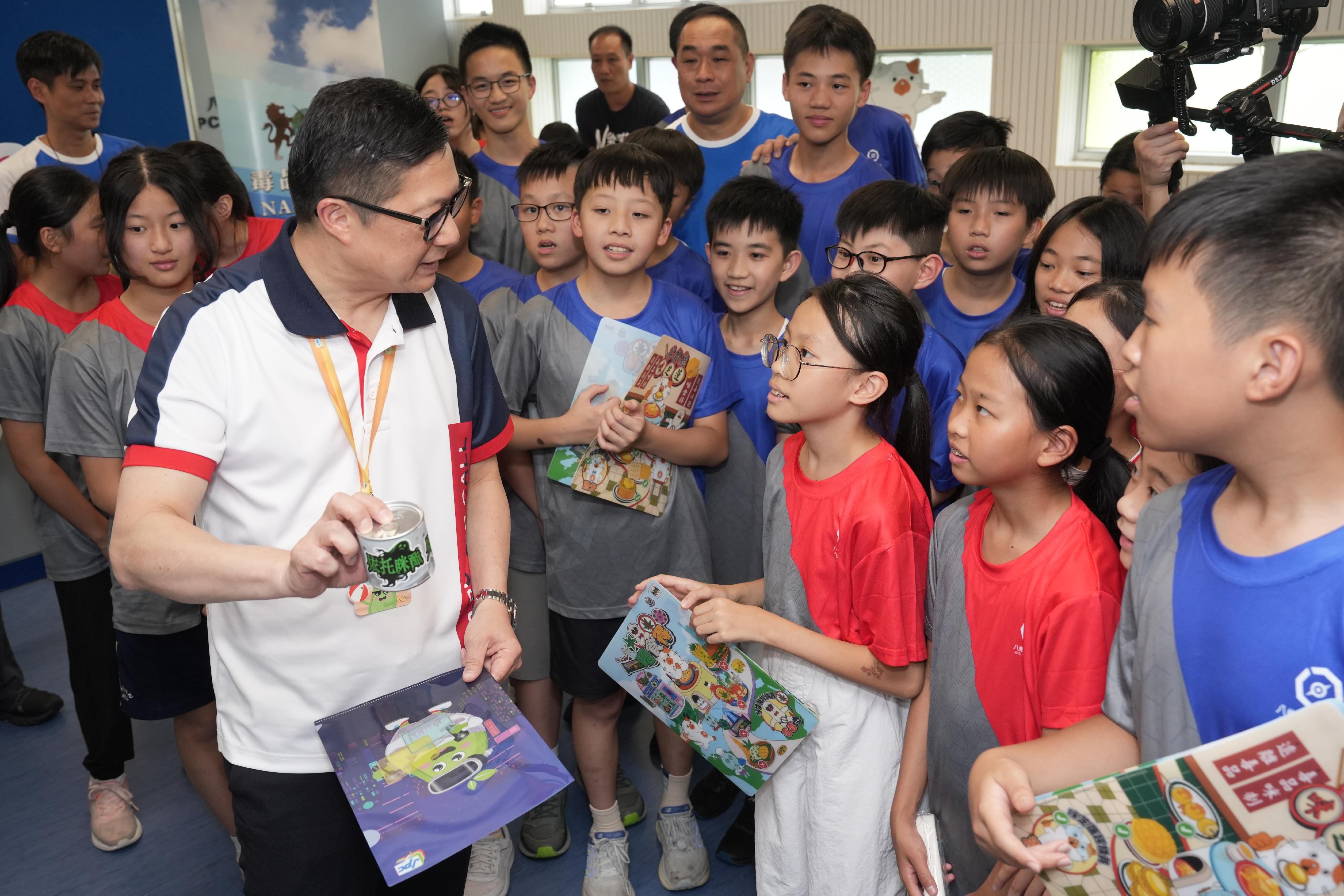 「少年警訊夏令營2025」開展禮今日（八月二十日）舉行。保安局局長暨少年警訊總名譽會長鄧炳強（前排左一）參觀警務處毒品調查科設置的攤位後，向少年警訊會員講解依托咪酯的禍害。
