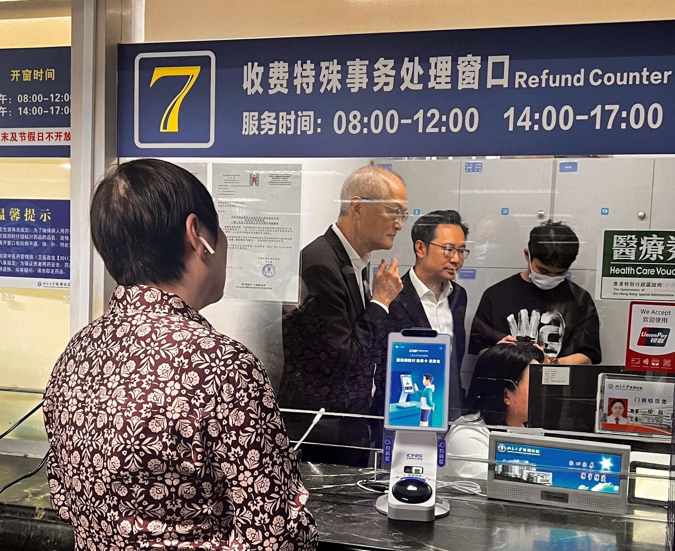 醫務衞生局（醫衞局）局長盧寵茂教授今日（八月二十八日）到北京大學深圳醫院視察首日推行「長者醫療券大灣區試點計劃」的運作安排。圖示盧寵茂教授（左）和醫衞局副秘書長李力綱（中）聽取院方講解香港長者結帳流程。

