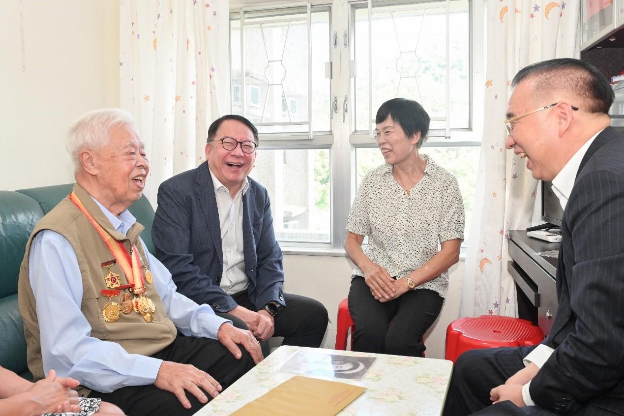 今年是中國人民抗日戰爭暨世界反法西斯戰爭勝利80周年，政務司司長陳國基和民政及青年事務局（民青局）局長麥美娟今日（八月二十九日）分別與中央人民政府駐香港特別行政區聯絡辦公室（中聯辦）副主任劉光源和中聯辦秘書長王松苗，上門探訪三位在港並曾參加抗戰的老兵，向他們表達慰問和關懷。圖示陳國基（左二）和劉光源（右一）與老兵及其家屬交談。