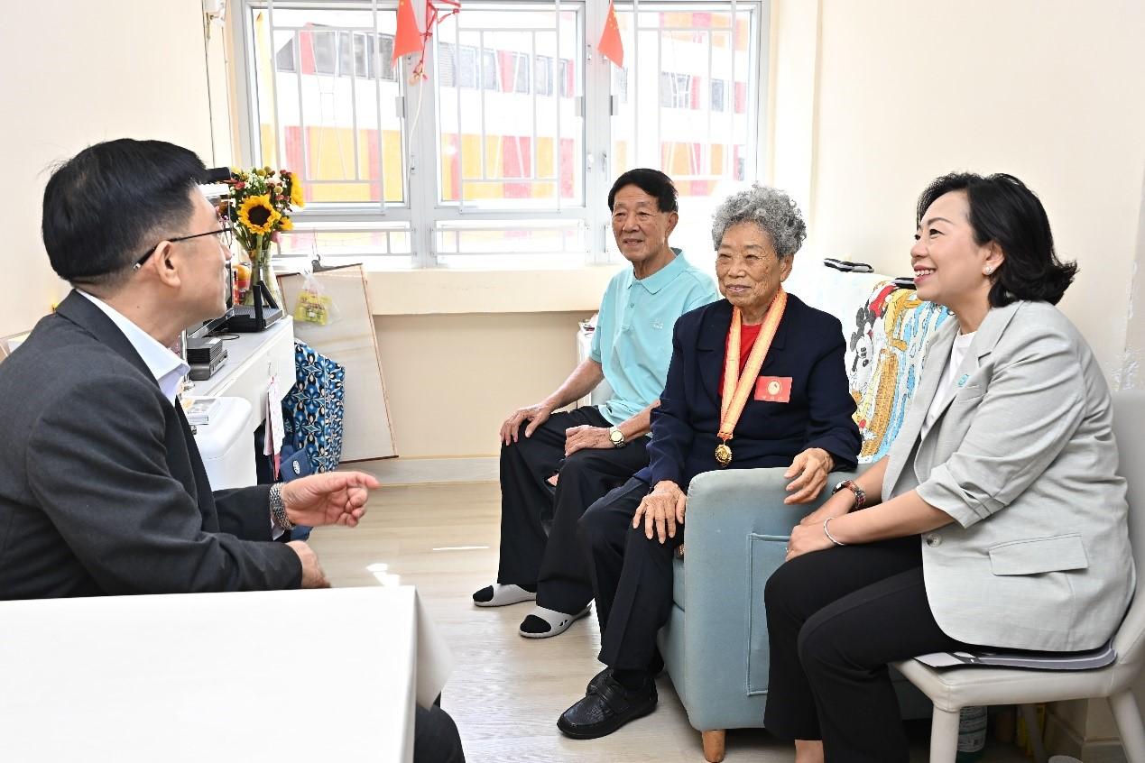 今年是中國人民抗日戰爭暨世界反法西斯戰爭勝利80周年，政務司司長陳國基和民政及青年事務局（民青局）局長麥美娟今日（八月二十九日）分別與中央人民政府駐香港特別行政區聯絡辦公室（中聯辦）副主任劉光源和中聯辦秘書長王松苗，上門探訪三位在港並曾參加抗戰的老兵，向他們表達慰問和關懷。圖示麥美娟（右一）和王松苗（左一）與老兵及其家屬交談。