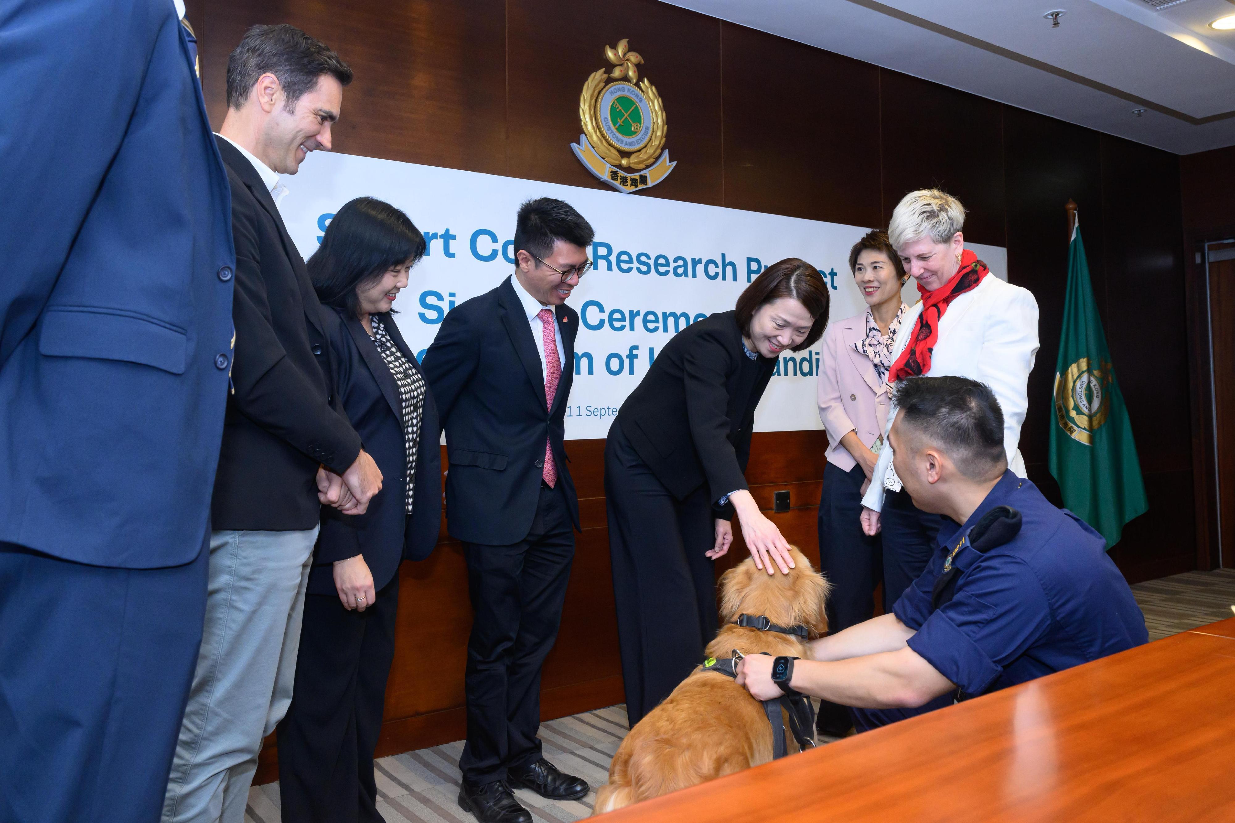 The Customs and Excise Department signed a Memorandum of Understanding to advance the operational effectiveness of Customs detector dogs through the Smart Collar Research Project with the City University of Hong Kong (CityU) today (September 11) at the Customs Headquarters Building. Photo shows the Assistant Commissioner (Boundary and Ports) of Customs and Excise, Ms Chiang Yi-lee (fourth right), with other Customs officials and representatives of CityU interacting with Customs detector dog after the signing ceremony of Memorandum of Understanding.