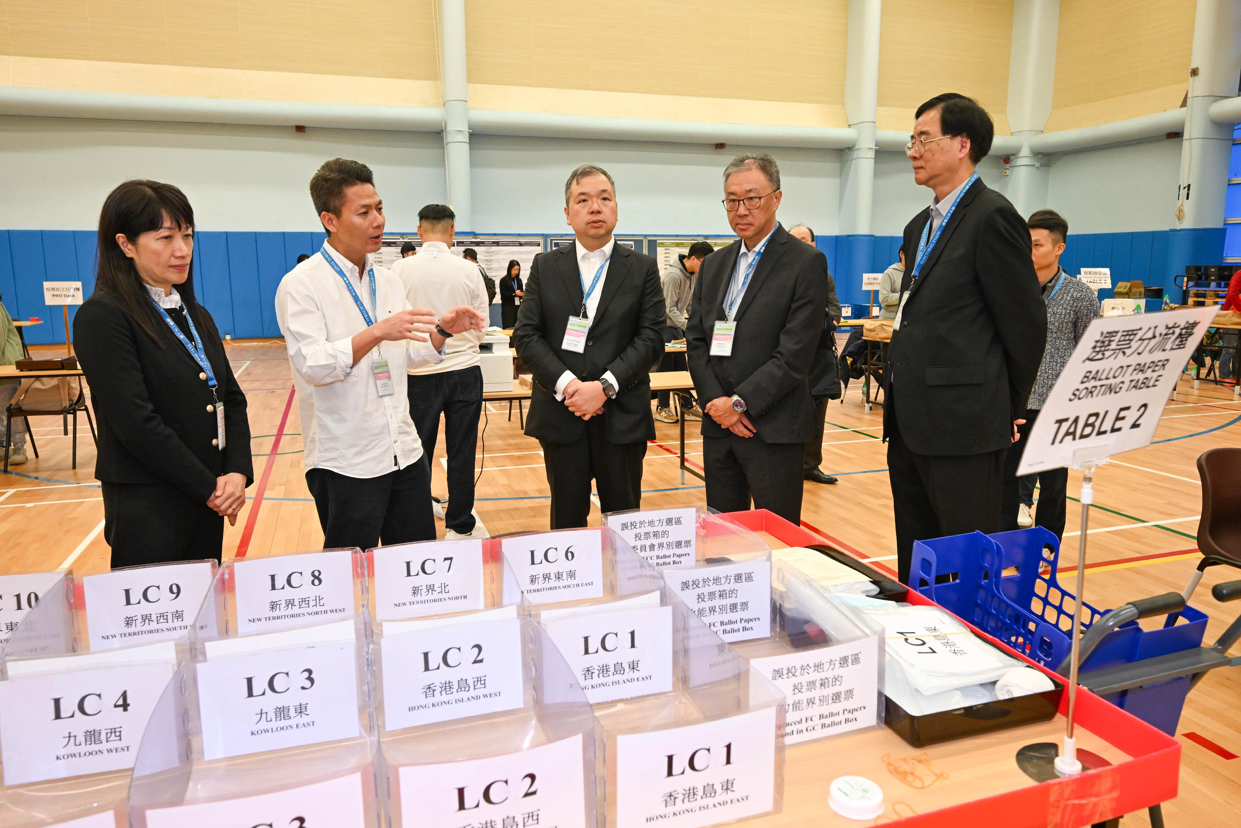 選舉管理委員會主席陸啟康法官(右二)、委員石丹理教授(右一)和文本立資深大律師(中)今日(十二月六日)下午到訪九龍公園體育館的選票分流站兼綜合大點票站,實地視察選舉工作人員的預備工作。旁為選舉事務處總選舉事務主任陳淑華(左一)。