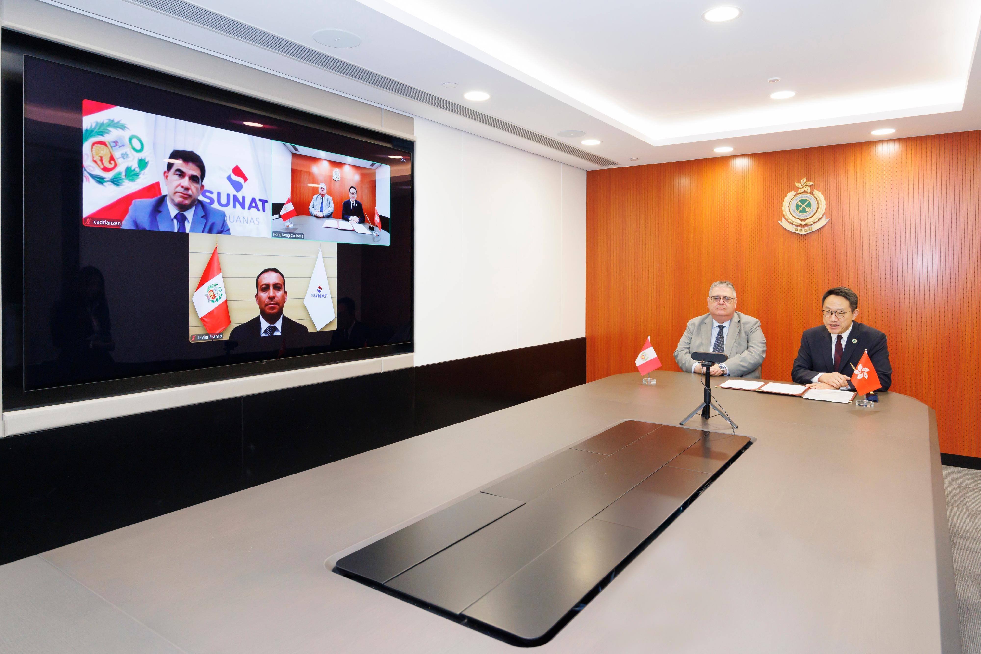 海關關長陳子達今日(十二月三十日)在香港海關總部大樓與秘魯海關稅務總局以線上線下模式達成「認可經濟營運商計劃」的互認安排。圖示陳子達(右)、秘魯駐港總領事Enrique Carlos Cardenas Arestegui(左)、秘魯海關稅務總局局長 Javier Franco Castillo(屏幕下)及秘魯海關稅務總局副局長Carlos Adrianzen(屏幕左上)以線上線下模式出席互認安排簽署儀式。
