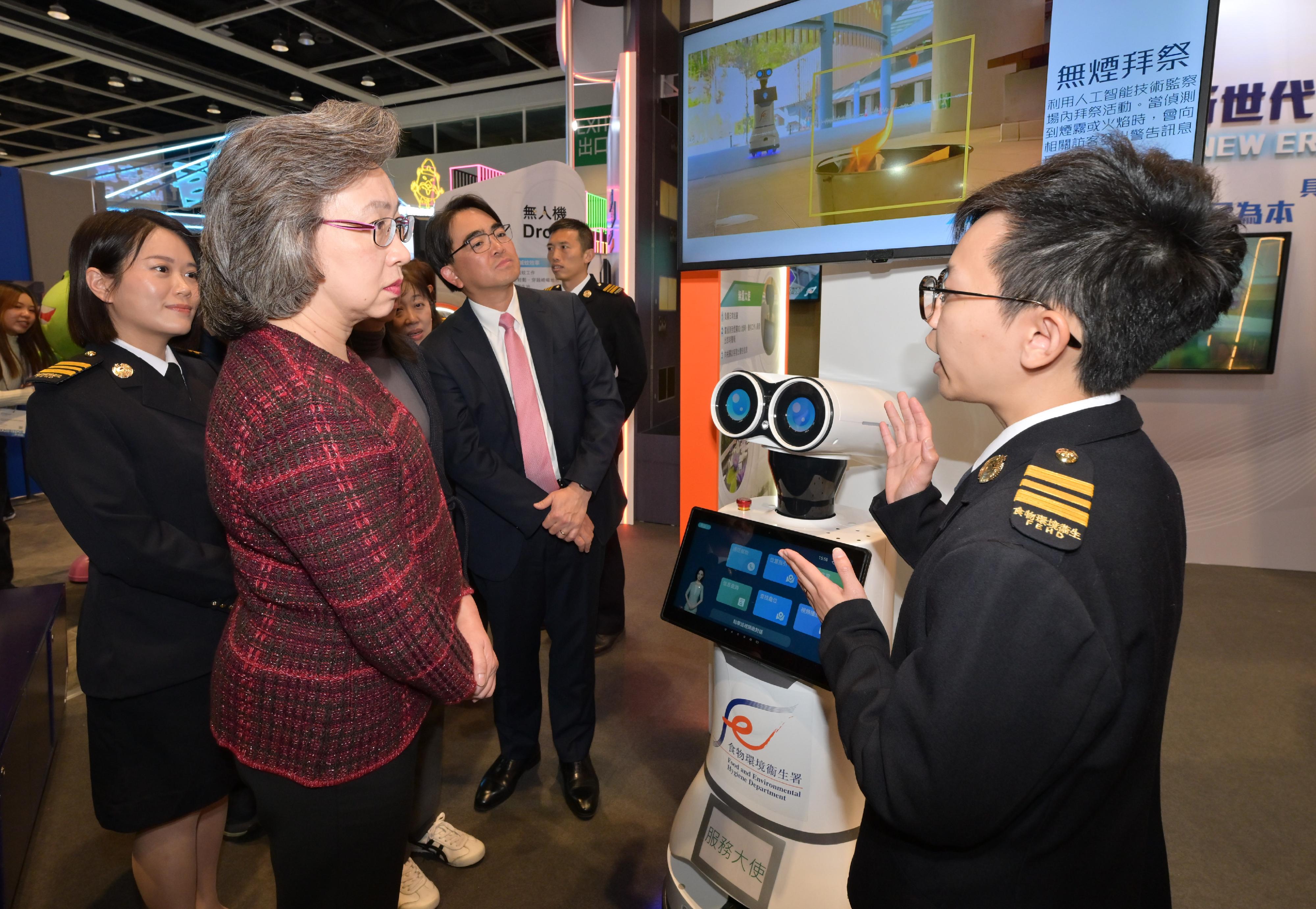 The Secretary for the Civil Service, Mrs Ingrid Yeung, today (January 22) visited the exhibition booths set up by various policy bureaux and departments at the Education & Careers Expo 2026. She encouraged students and young people to gain an understanding of the diverse work and career opportunities across different government departments, and to consider joining the Government to build the future of Hong Kong together. Photo shows Mrs Yeung (second left) being briefed on the robot equipped with artificial intelligence to enforce the "smoke-free worship" requirement by an officer of the Food and Environmental Hygiene Department at the department's booth. Looking on is the Director of Food and Environmental Hygiene, Mr Donald Ng (third left).