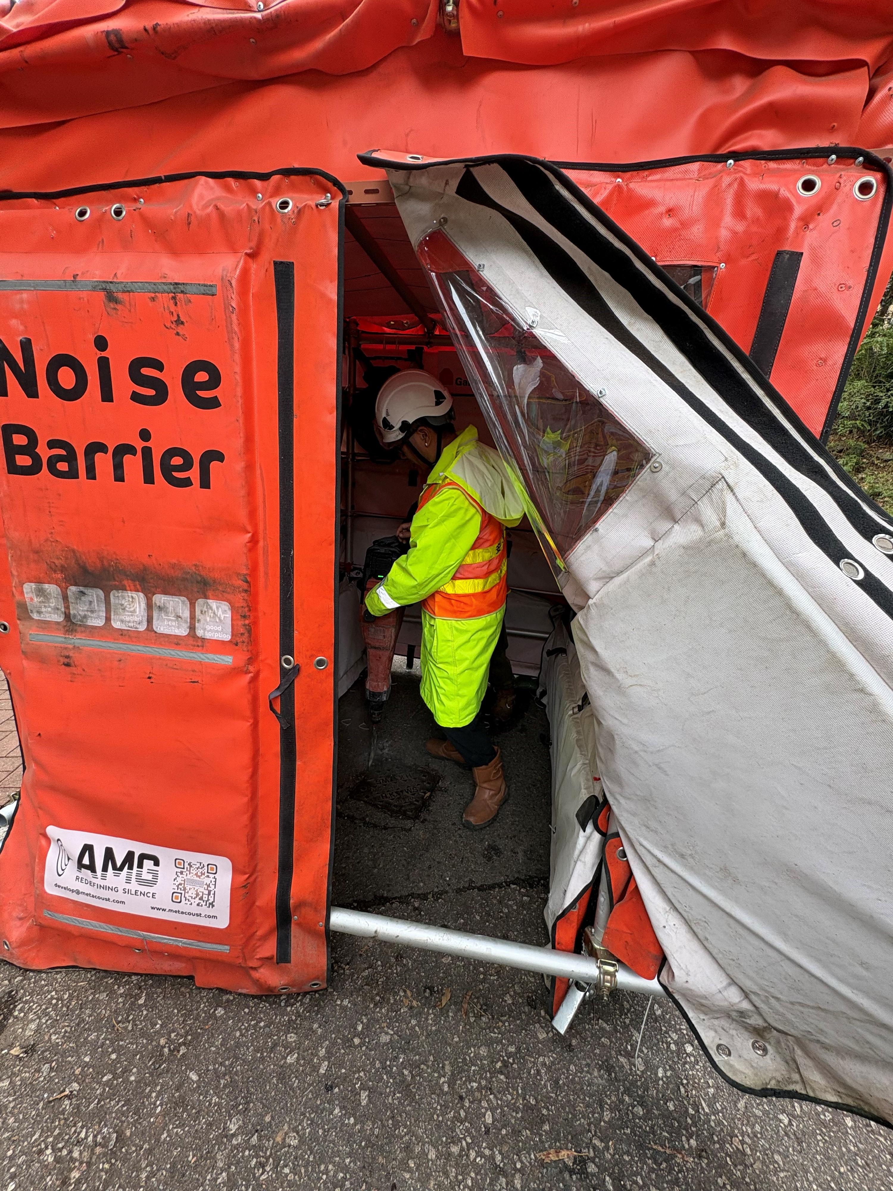 環境保護署今日（二月六日）表示，透過與路政署協作，將由塑膠回收再造成的創新聲學超材料應用於路政署在大埔運頭角里的一項道路重鋪工程，顯著減少工程噪音對鄰近居民的影響，成功將原先施工時間由三晚壓縮至一整天。圖示工人模擬在聲學超材料隔音罩內打鑿路面。