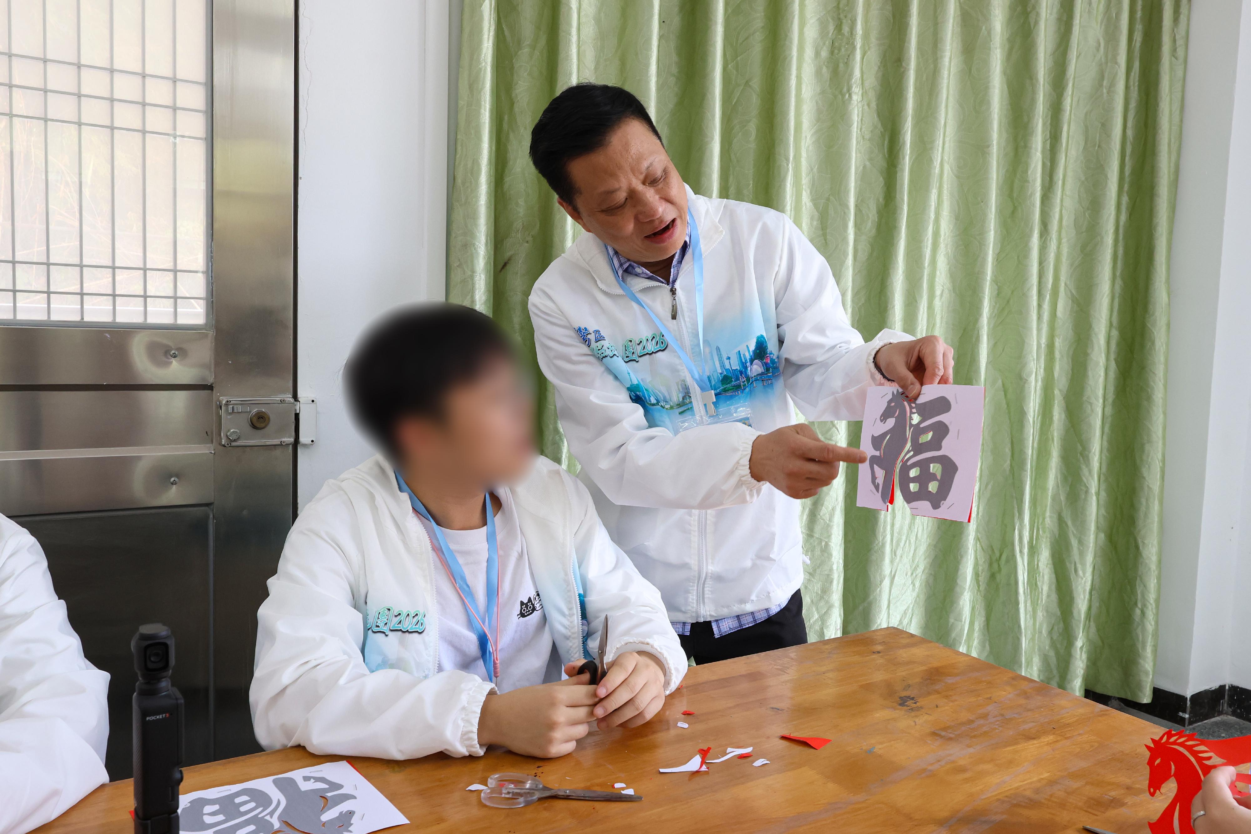 To further cultivate national consciousness and positive values in young rehabilitated persons, correctional officers led youths who have completed their sentences and are under statutory supervision to participate in the Greater Bay Area Experience Exchange Tour 2026, visiting Foshan and Zhuhai in the Guangdong-Hong Kong-Macao Greater Bay Area for three days and two nights of exchanges, so that they could learn about the country's history and culture as well as its developments in various fields. Photo shows the tour's sponsor, Mr Ha Chung-kin (right), leading a young rehabilitated person to experience the making of Chinese traditional handicraft at a school in Foshan on February 7, enabling him to understand the profound Chinese history and culture.
