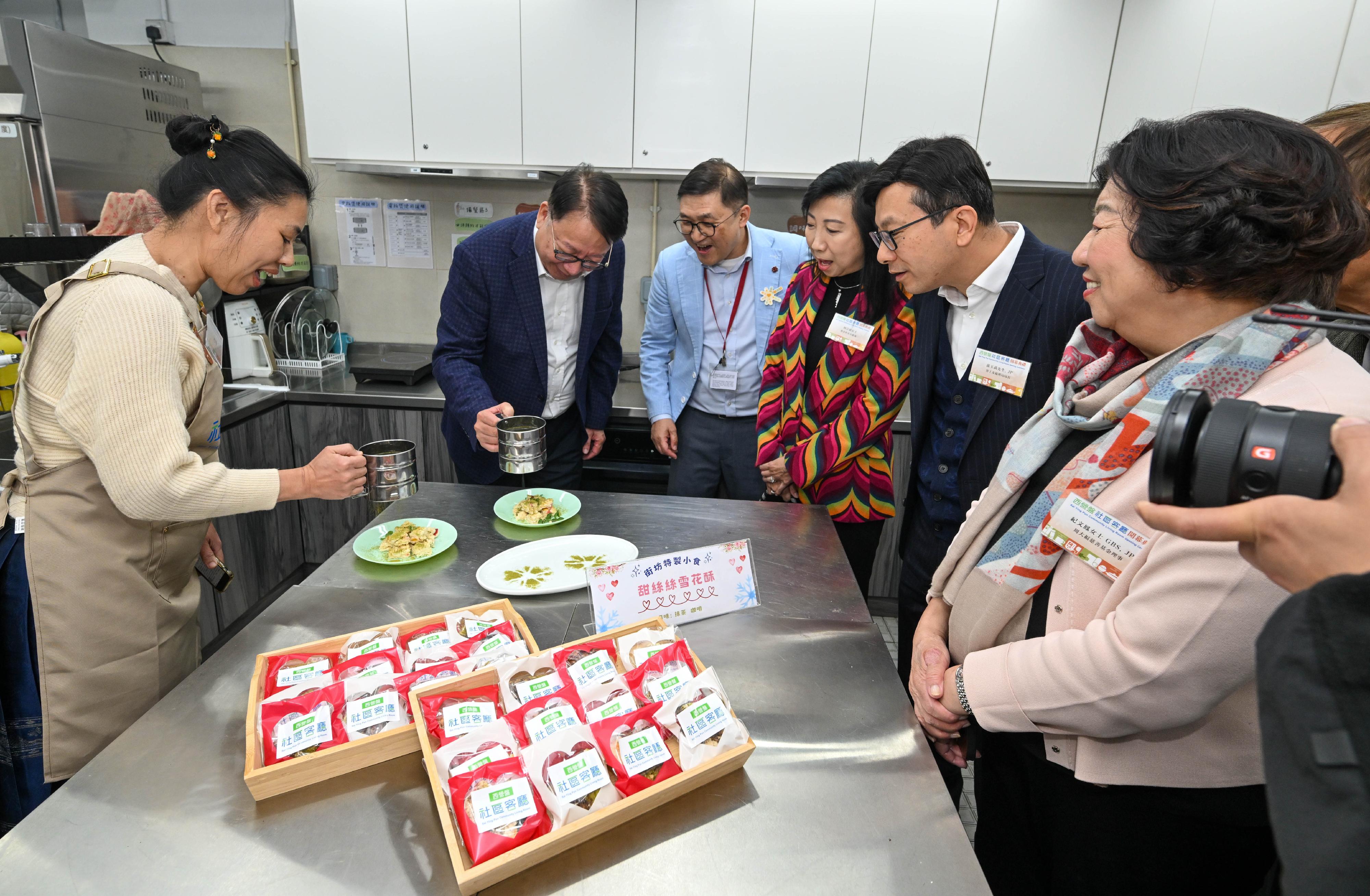 政務司司長陳國基今日（二月九日）主持西營盤社區客廳開幕典禮。勞工及福利局局長孫玉菡、周大福慈善基金理事紀文鳳、利希慎基金總裁何宗慈、勞工及福利局常任秘書長劉焱、社會福利署署長杜永恒和香港明愛總裁閻德龍神父亦一同主禮。圖示陳國基（左二）和孫玉菡（右二）在鄰里備餐區與受惠家庭製作小食。