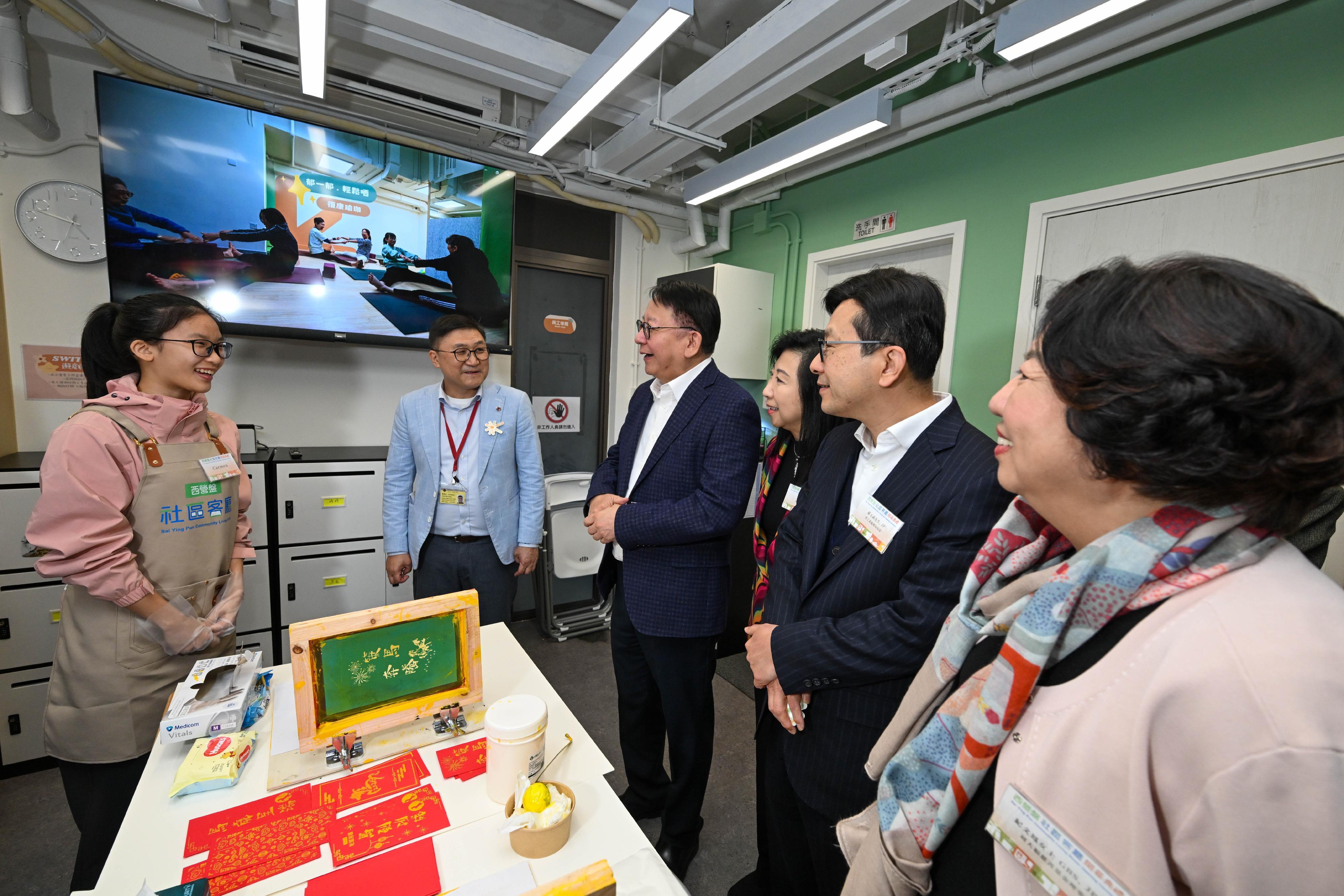 政務司司長陳國基今日（二月九日）主持西營盤社區客廳開幕典禮。勞工及福利局局長孫玉菡、周大福慈善基金理事紀文鳳、利希慎基金總裁何宗慈、勞工及福利局常任秘書長劉焱、社會福利署署長杜永恒和香港明愛總裁閻德龍神父亦一同主禮。圖示陳國基（左三）和孫玉菡（右二）與正在製作絲網印刷利是封的用戶交流。