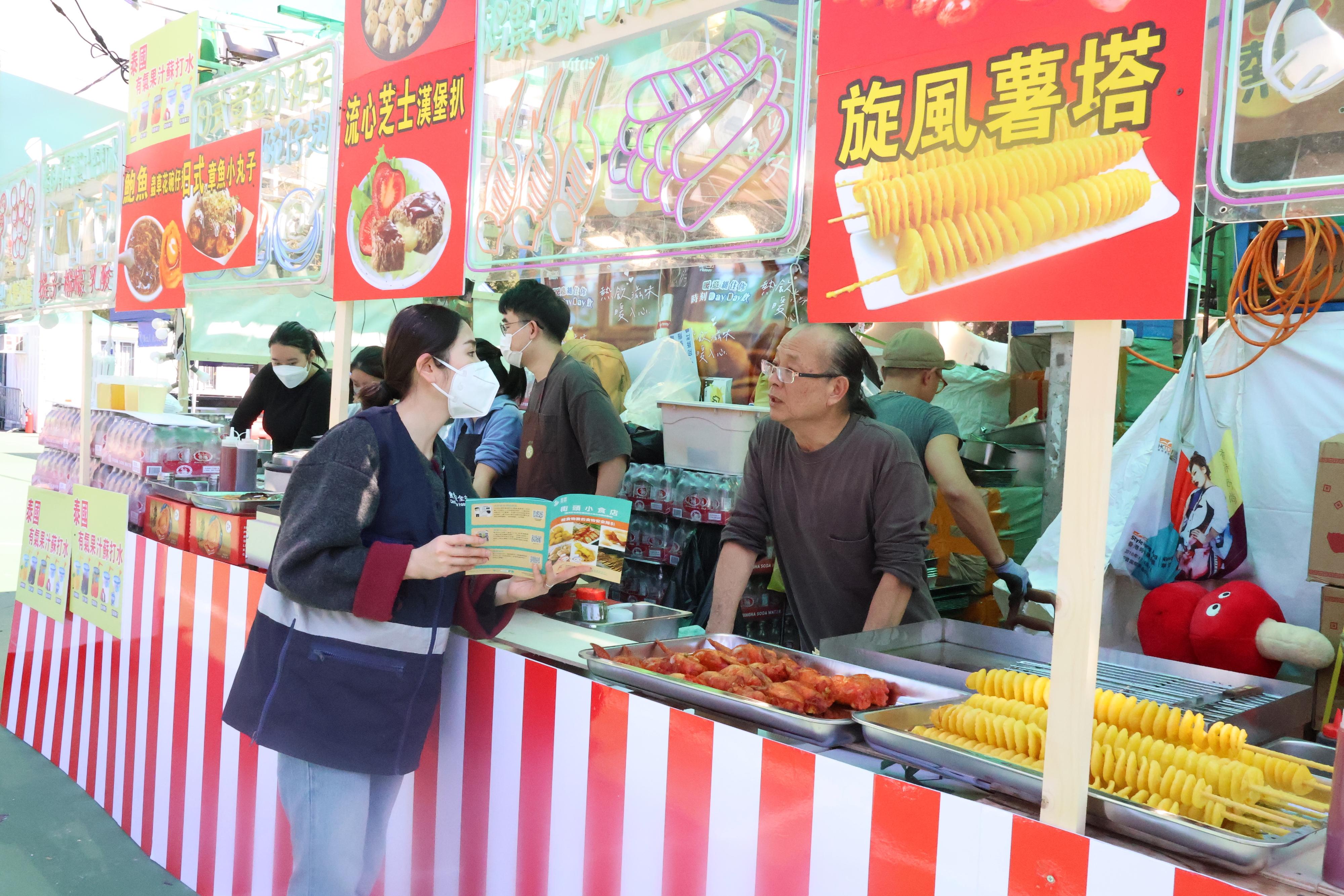 The 2026 Lunar New Year (LNY) fairs are being held at 14 locations across the territory. The Centre for Food Safety (CFS) of the Food and Environmental Hygiene Department has arranged for staff to inspect the fast food stalls at LNY fairs. Photo shows a CFS officer providing health education on food safety and hygiene and distributing booklets to remind fast food stall operators of food safety.
