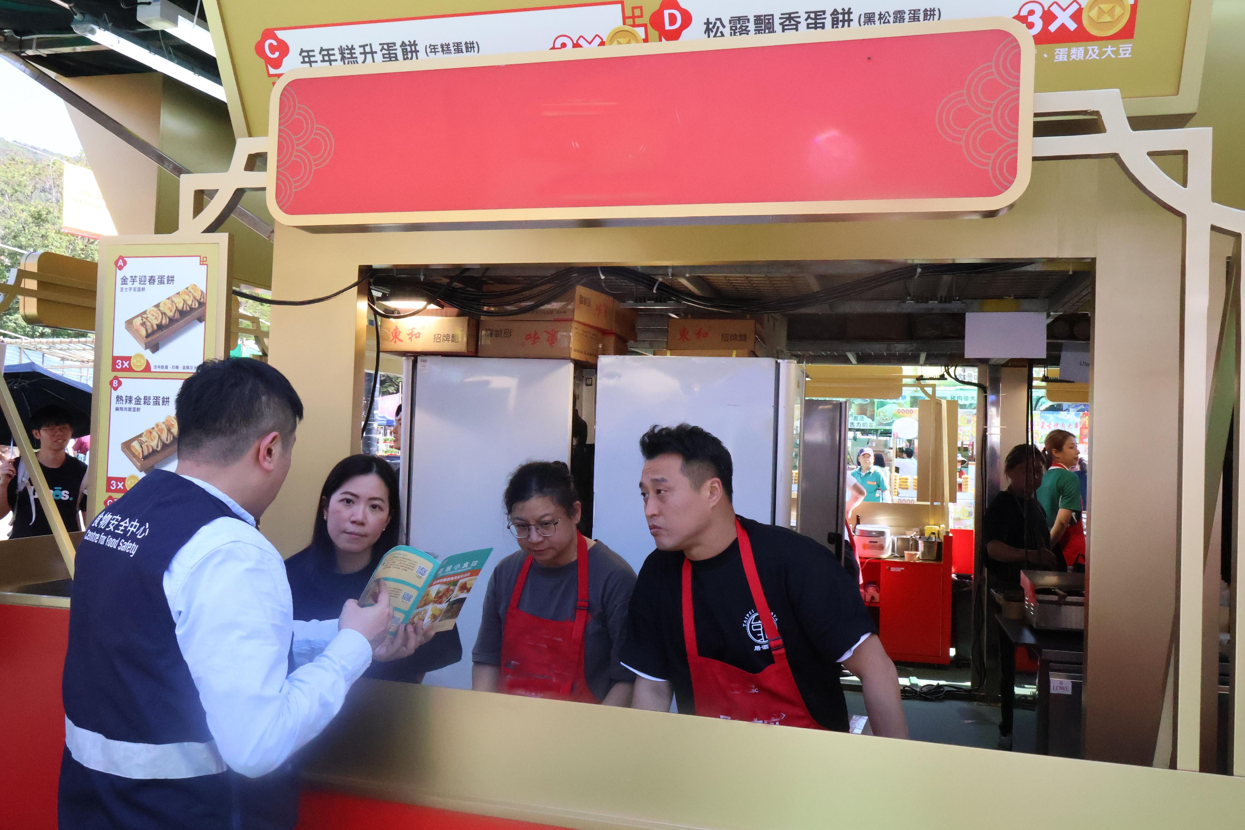 The 2026 Lunar New Year (LNY) fairs are being held at 14 locations across the territory. The Centre for Food Safety (CFS) of the Food and Environmental Hygiene Department has arranged for staff to inspect the fast food stalls at LNY fairs. Photo shows a CFS officer providing health education on food safety and hygiene and distributing booklets to remind fast food stall operators of food safety.