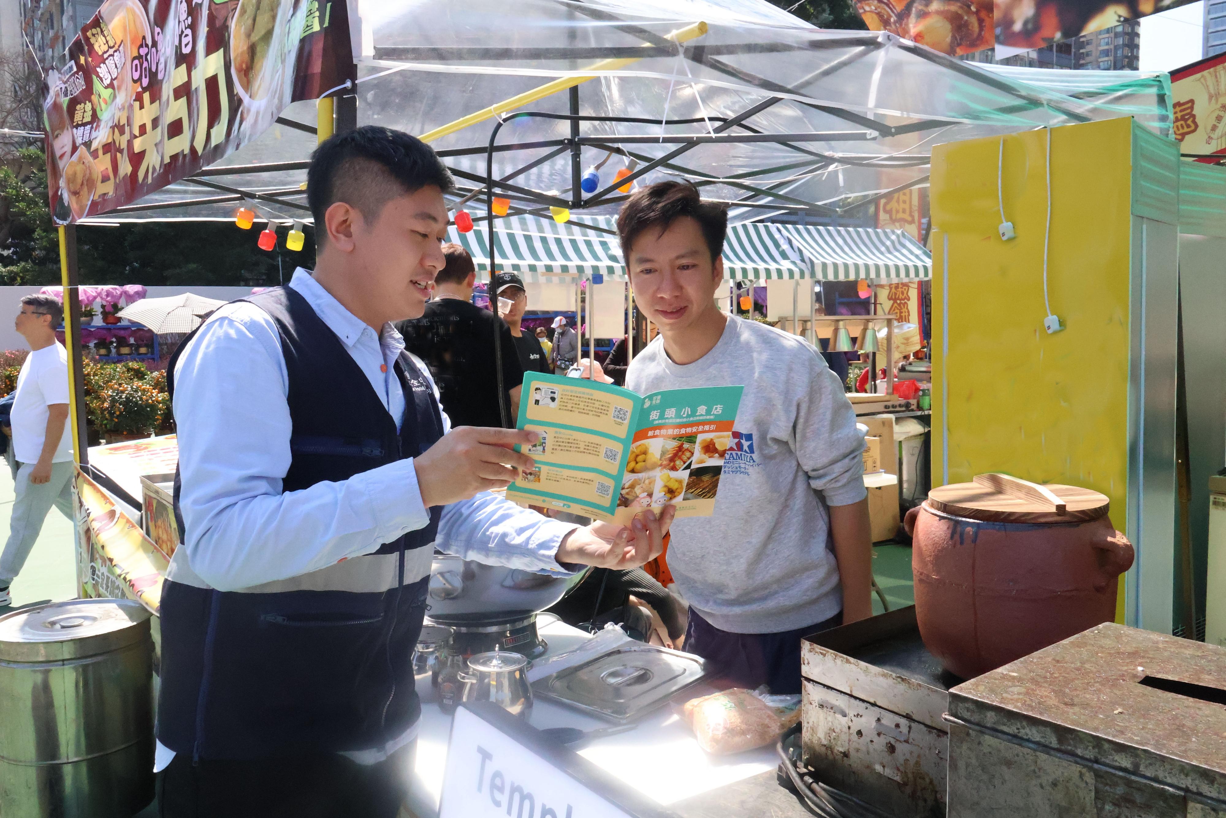 The 2026 Lunar New Year (LNY) fairs are being held at 14 locations across the territory. The Centre for Food Safety (CFS) of the Food and Environmental Hygiene Department has arranged for staff to inspect the fast food stalls at LNY fairs. Photo shows a CFS officer providing health education on food safety and hygiene and distributing booklets to remind fast food stall operators of food safety.