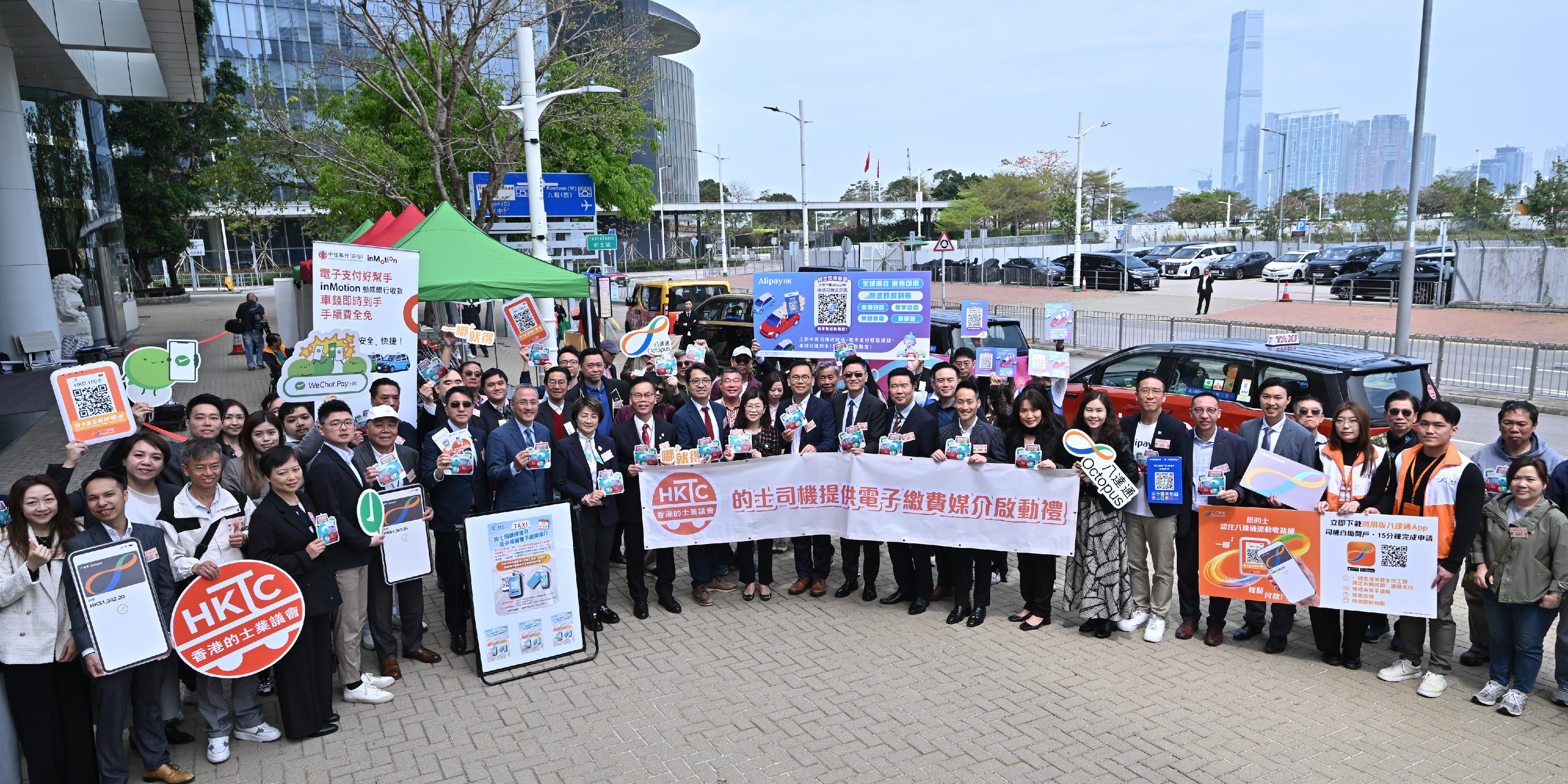 運輸署今日（三月十五日）提醒的士司機，由今年四月一日起，必須提供電子繳費媒介，以方便乘客繳付車費。乘客登車前，可留意車窗貼紙或向司機了解所提供的電子繳費媒介。乘客亦可繼續以現金繳費。圖示運輸署助理署長／管理及輔助客運馮惠筠（前排中）聯同立法會議員，以及相關部門、機構及主要電子繳費平台代表出席的士業界宣傳活動，呼籲尚未安裝電子繳費媒介的司機盡快安裝並熟習操作。
