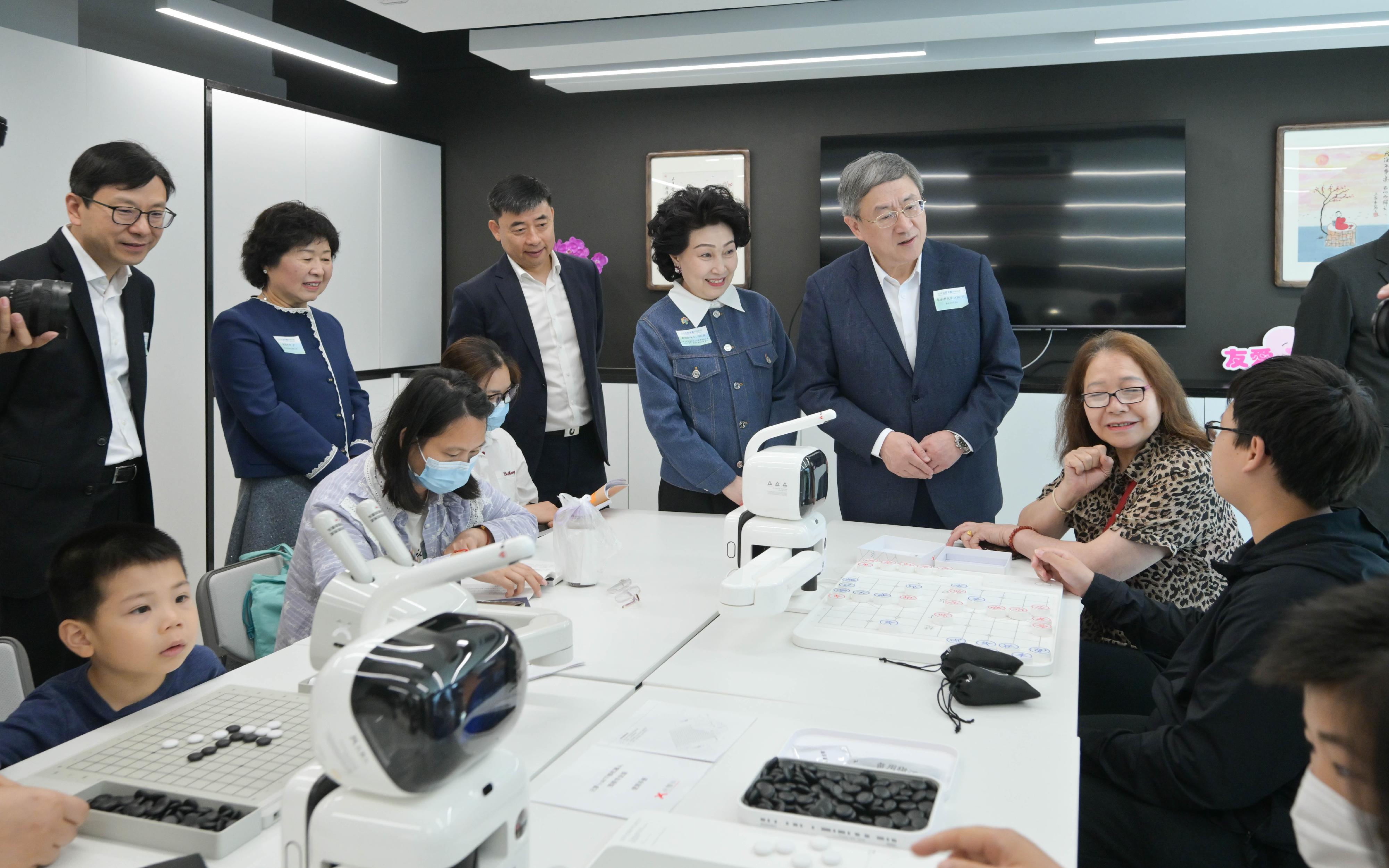 署理政務司司長卓永興今日（三月三十日）主持旺角社區客廳開幕典禮。中央人民政府駐香港特別行政區聯絡辦公室副主任羅永綱及勞工及福利局局長孫玉菡亦一同主禮。圖示卓永興（站立，右一）和孫玉菡（站立，左一）與正在體驗AI智能下棋活動的受惠家庭交流。