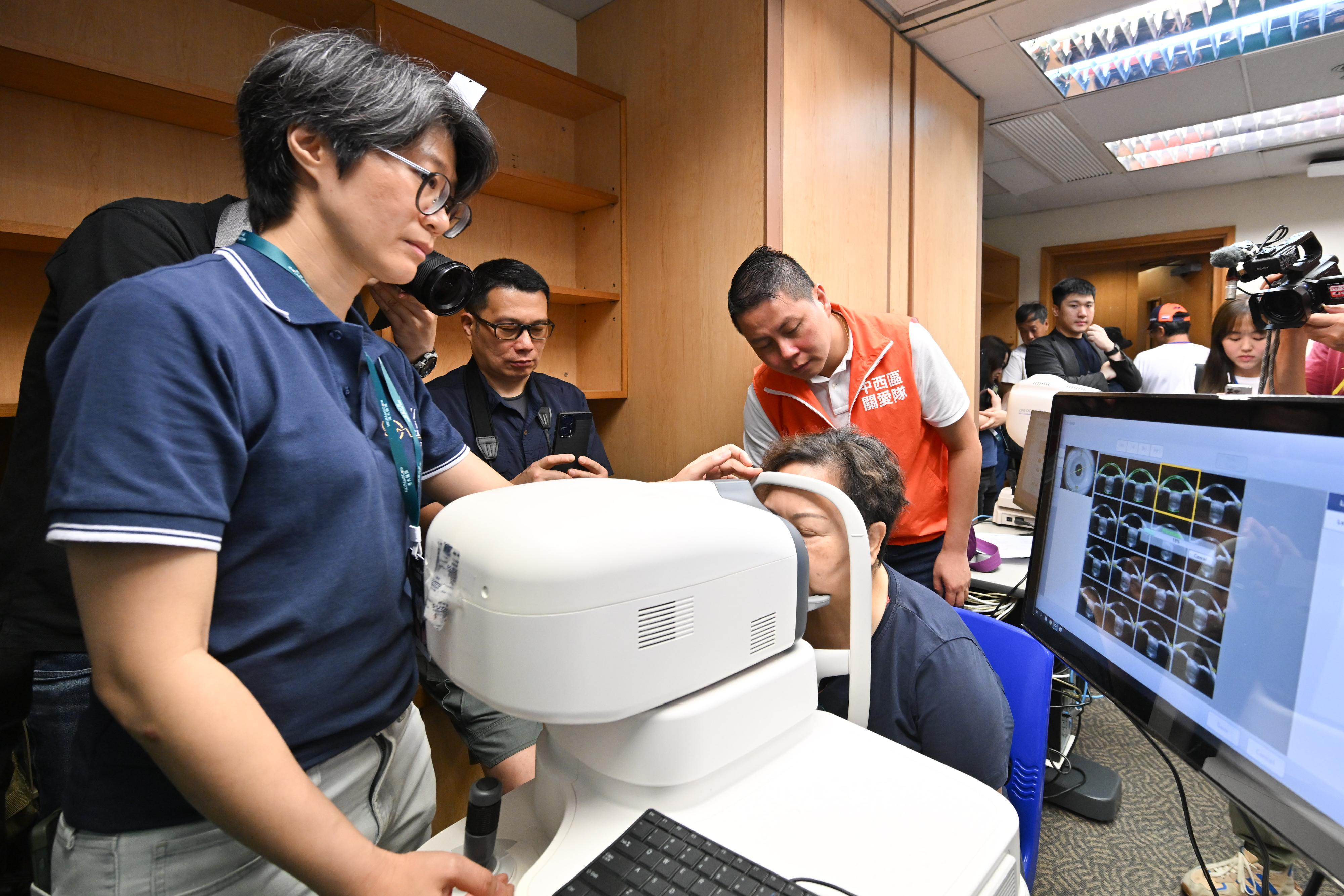 The Home and Youth Affairs Bureau, the District Services & Community Care Teams (Care Teams), and the Li Ka Shing Faculty of Medicine of the University of Hong Kong held the kick-off ceremony of the "Shape Your Healthy Life: 18 District Health Community Project" and the first district outreach health promotion event at the Sai Ying Pun Community Complex Community Hall today (April 7). Photo shows a member of the Care Teams accompanying a participant for an eye examination.