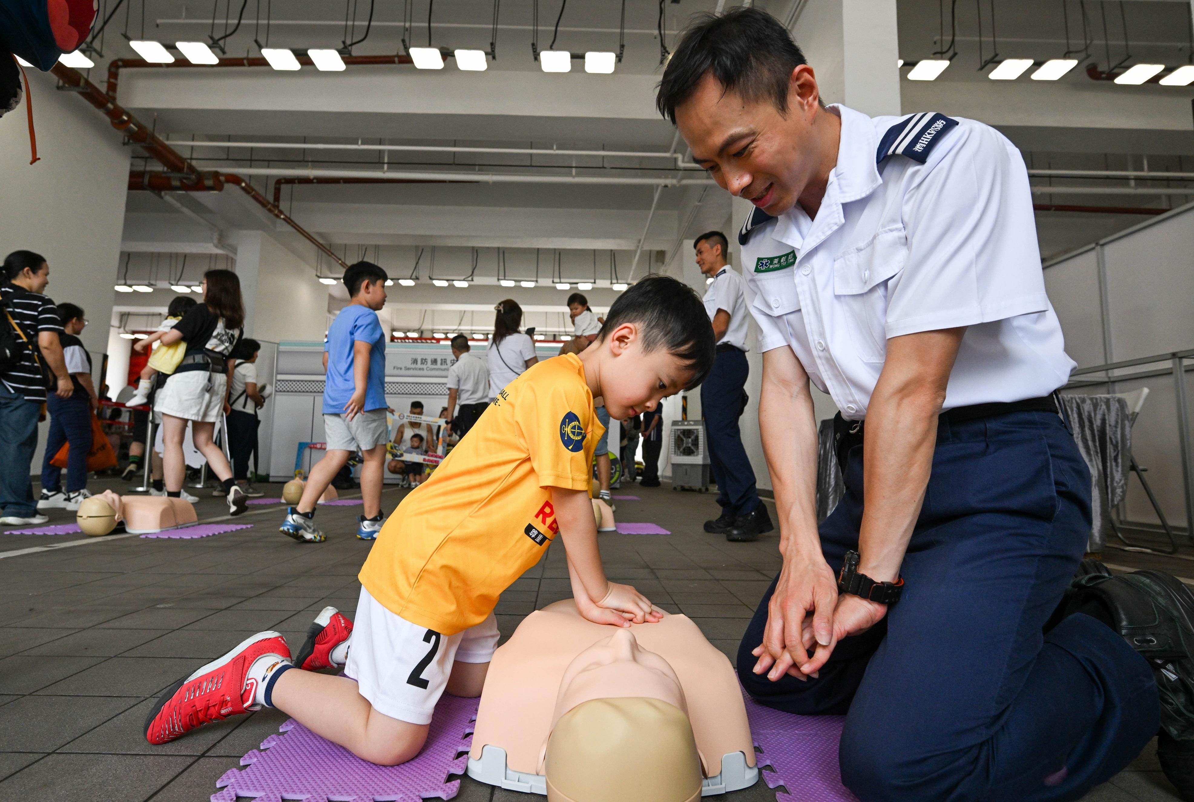 In response to and in support of the 11th National Security Education Day, the Fire Services Department held an open day at the Fire and Ambulance Services Academy in Tseung Kwan O today (April 12). Photo shows a child learning administration of cardiopulmonary resuscitation under the instruction of an ambulance officer.
