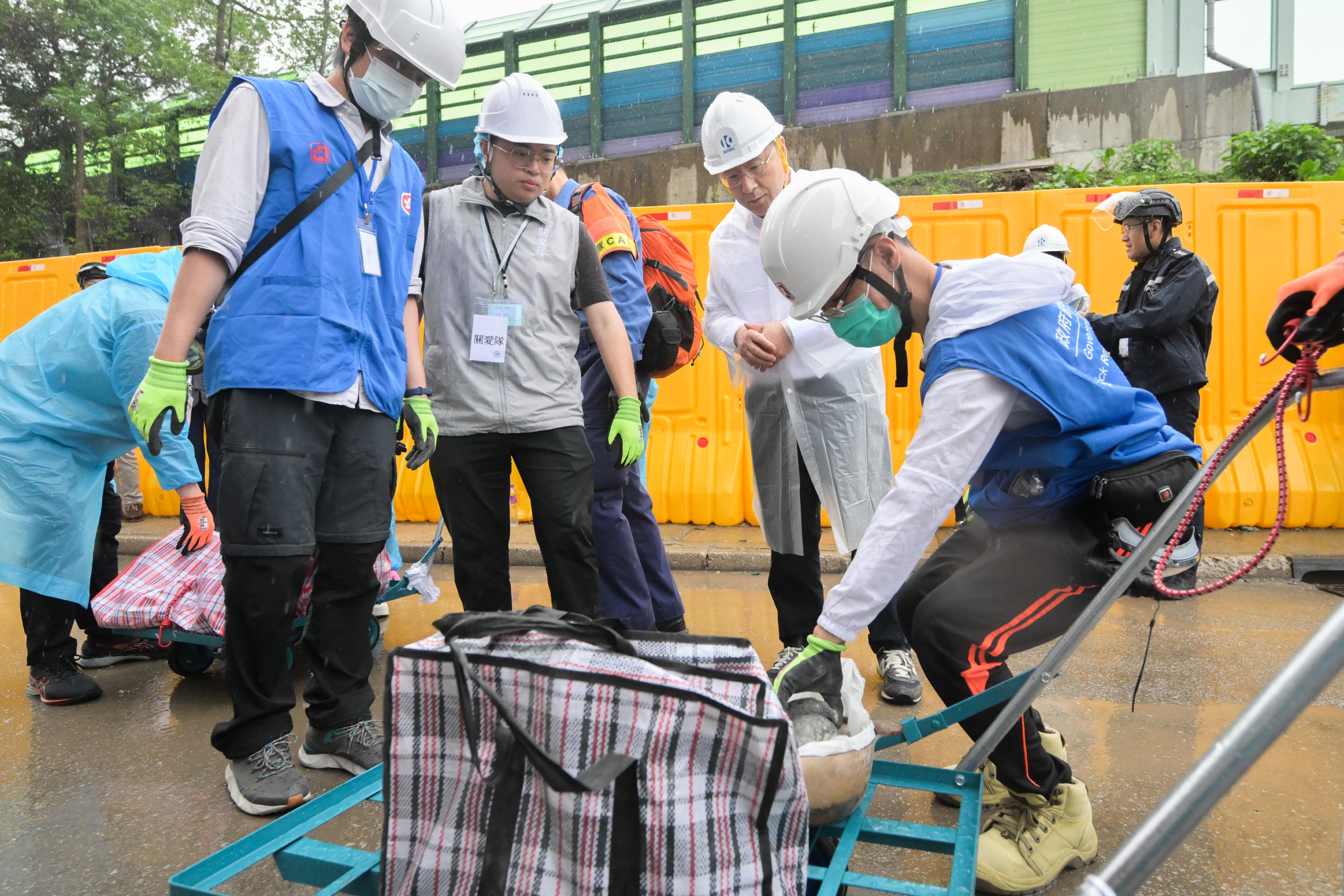 The Deputy Chief Secretary for Administration, Mr Cheuk Wing-hing, conducted a site visit to Wang Fuk Court in Tai Po today (April 24) to inspect the second round of arrangements for the opening of two buildings in parallel, as well as the wet weather operations. Mr Cheuk first observed the resident waiting area set up at Tai Po Baptist Public School to learn about the support that the Home Affairs Department provided to residents waiting to return to their units, and the arrangements of a vehicle-booking service. Later he visited the on-site storage area to gain an understanding of the utilisation situation of the temporary storage service after opening two buildings at the same time. Subsequently, accompanied by Deputy Director of Home Affairs Ms Belinda Wong and the District Commander of Tai Po District, Mr Kong Wing-cheung, Mr Cheuk observed police officers, Civil Aid Service members, and mobilised civil servants, along with District Services and Community Care Team volunteers, working together to assist residents in transporting their belongings in the vicinity of Wang Cheong House. Mr Cheuk thanked all those involved in the support service for their enthusiasm and willingness to go the extra mile, ensuring the smooth progress of the access arrangements. Photo shows Mr Cheuk (second right) talking with civil servants mobilised from the Electrical and Mechanical Services Department in the vicinity of Wang Cheong House.