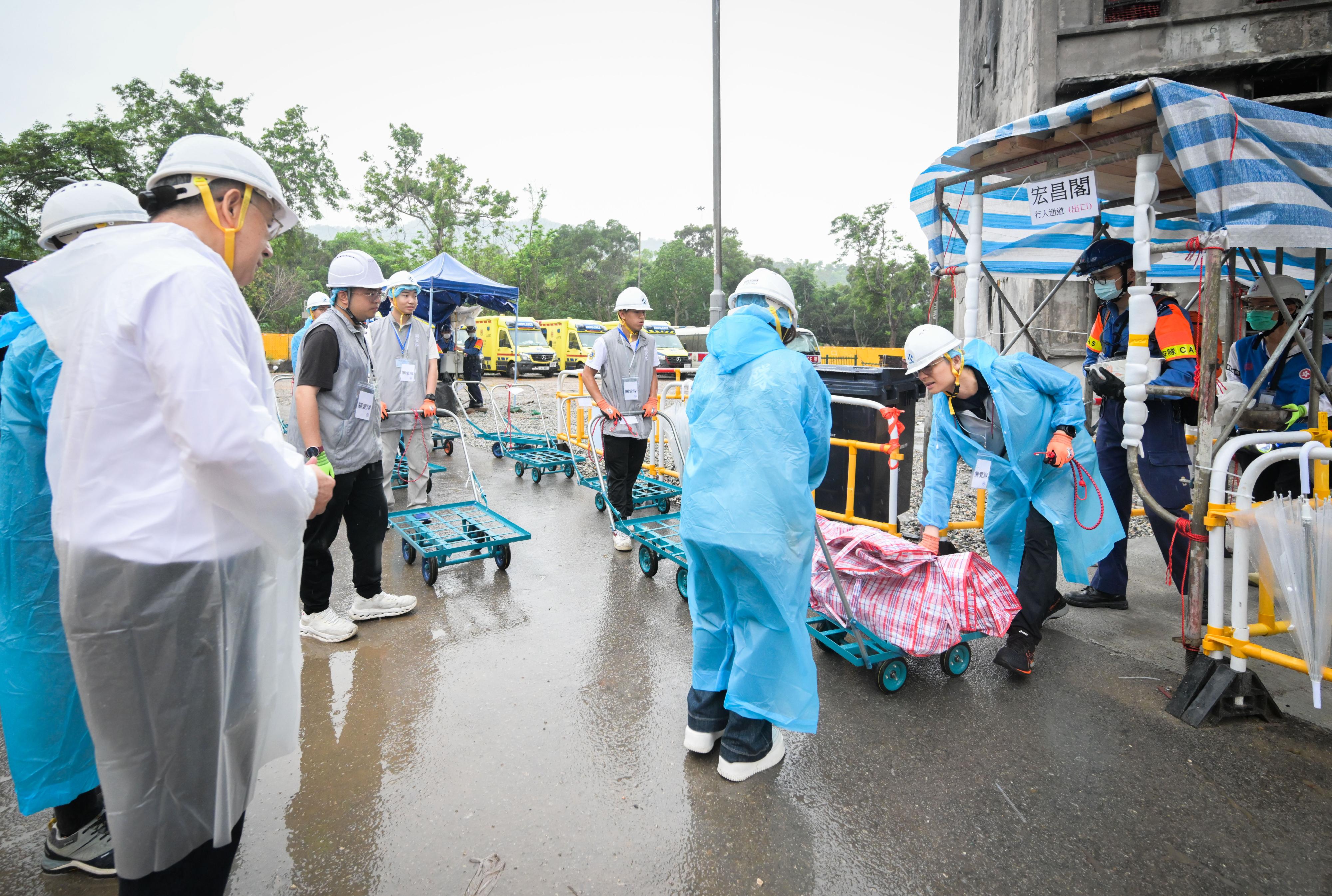 The Deputy Chief Secretary for Administration, Mr Cheuk Wing-hing, conducted a site visit to Wang Fuk Court in Tai Po today (April 24) to inspect the second round of arrangements for the opening of two buildings in parallel, as well as the wet weather operations. Mr Cheuk first observed the resident waiting area set up at Tai Po Baptist Public School to learn about the support that the Home Affairs Department provided to residents waiting to return to their units, and the arrangements of a vehicle-booking service. Later he visited the on-site storage area to gain an understanding of the utilisation situation of the temporary storage service after opening two buildings at the same time. Subsequently, accompanied by Deputy Director of Home Affairs Ms Belinda Wong and the District Commander of Tai Po District, Mr Kong Wing-cheung, Mr Cheuk observed police officers, Civil Aid Service members, and mobilised civil servants, along with District Services and Community Care Team volunteers, working together to assist residents in transporting their belongings in the vicinity of Wang Cheong House. Mr Cheuk thanked all those involved in the support service for their enthusiasm and willingness to go the extra mile, ensuring the smooth progress of the access arrangements. Photo shows Mr Cheuk (left) watching members of the Civil Aid Service and mobilised civil servants, along with volunteers of the District Services and Community Care Teams, helping residents move their belongings.