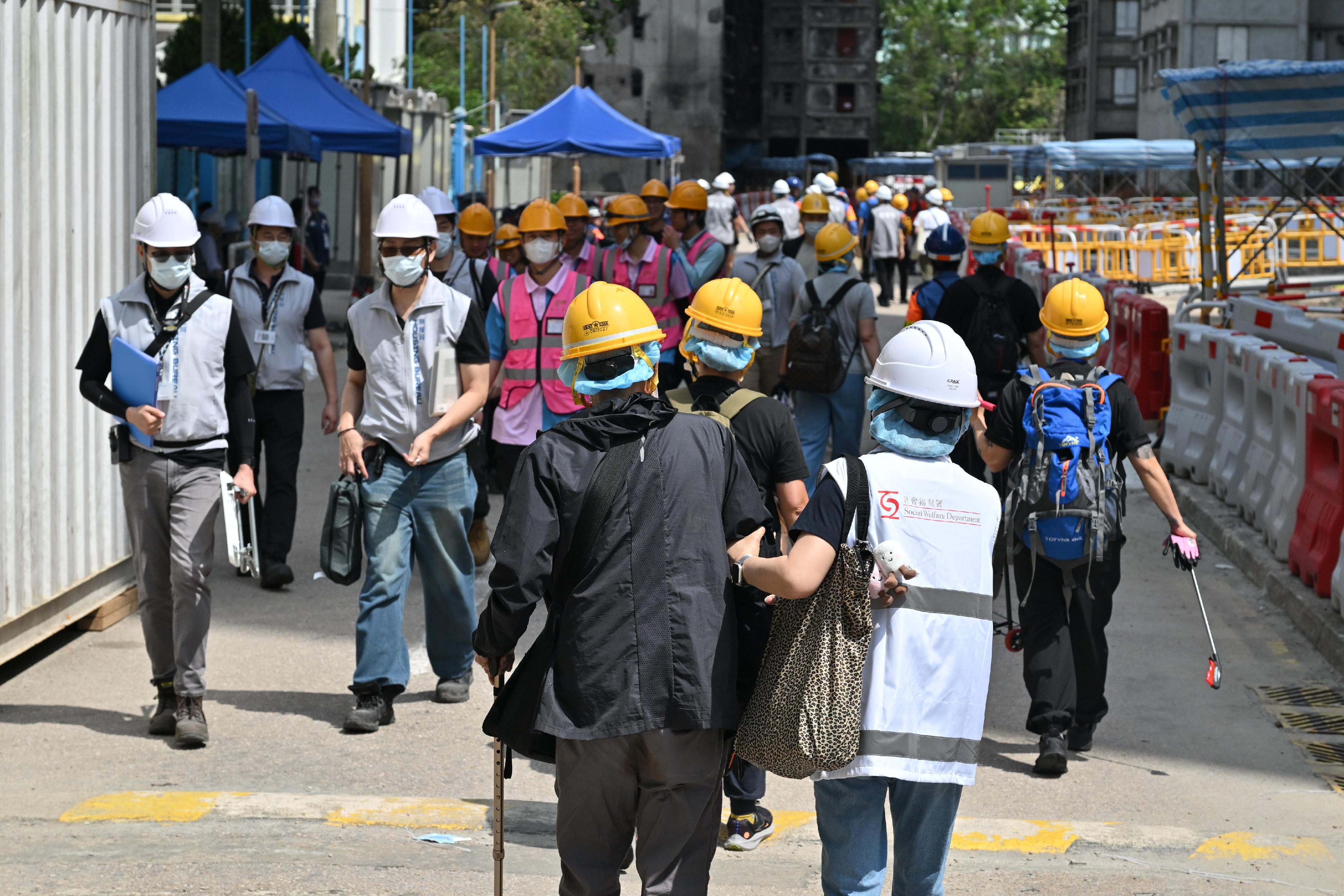 就今次宏福苑居民上樓安排，社會福利署派出1700多名「一戶一社工」為每個住戶提供支援，另外安排社工和臨床心理學家在開放的樓層組成專隊協助居民，亦會陪同有特別需要的居民（當中包括死者家屬）返回單位。圖示社工陪同上樓居民進入屋苑。
