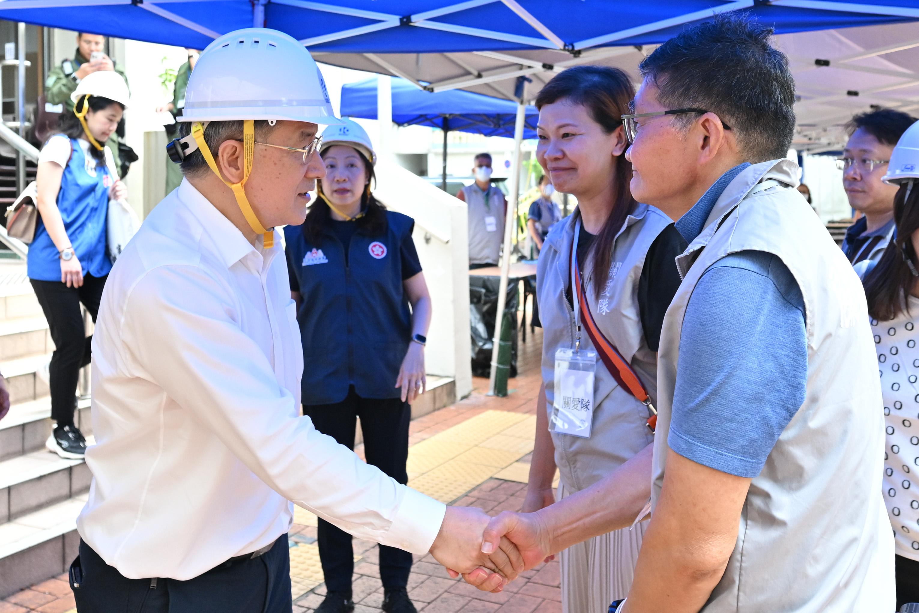 The Deputy Chief Secretary for Administration, Mr Cheuk Wing-hing (left), today (April 29) shakes hands with volunteers from the District Services and Community Care Teams at the personal protective equipment donning area at Kwong Fuk Community Hall in Tai Po, where they assist residents returning to their units.