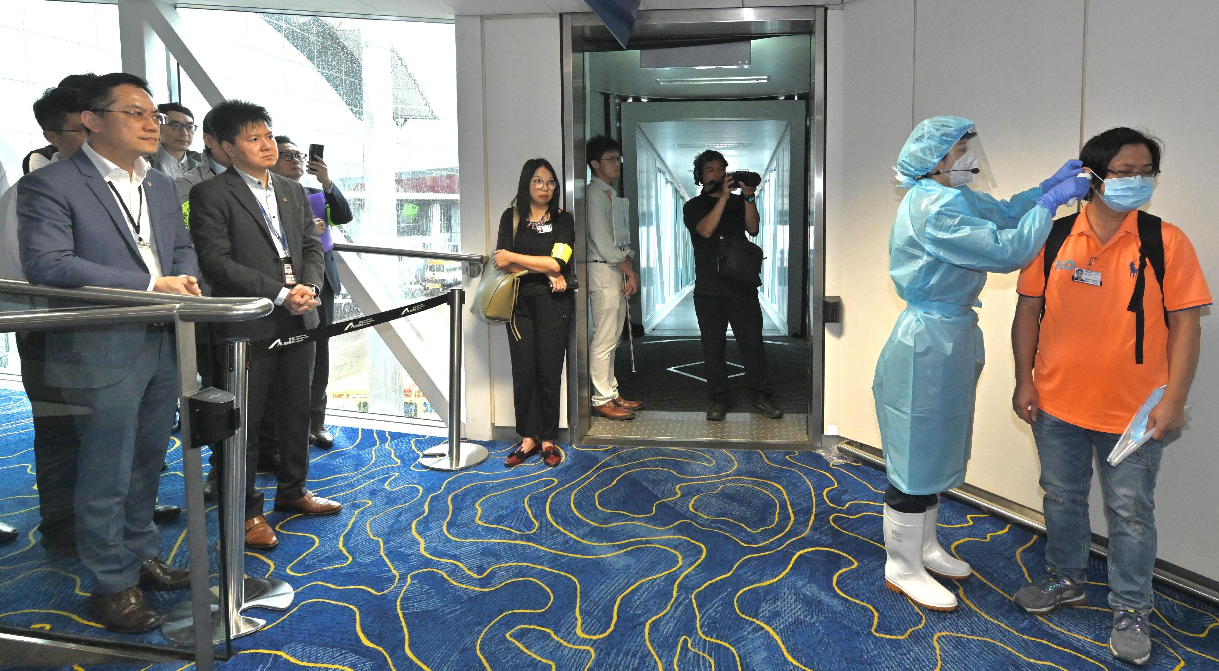 The Centre for Health Protection (CHP) of the Department of Health (DH) today (June 16) conducted a public health exercise codenamed "Charoite" in collaboration with various relevant government departments and organisations to strengthen stakeholders' response and co-ordination capabilities in handling suspected imported cases of Ebola disease and to enhance awareness among all units about the prevention and management of public health emergencies. Photo shows a Port Health Division officer under the CHP conducting a temperature check for a passenger exhibiting symptoms at a flight gate of Hong Kong International Airport in a simulated scenario. Looking on are the Director of Health, Dr Ronald Lam (first left), the Controller of the CHP of the DH, Dr Edwin Tsui (second left), and other observers.