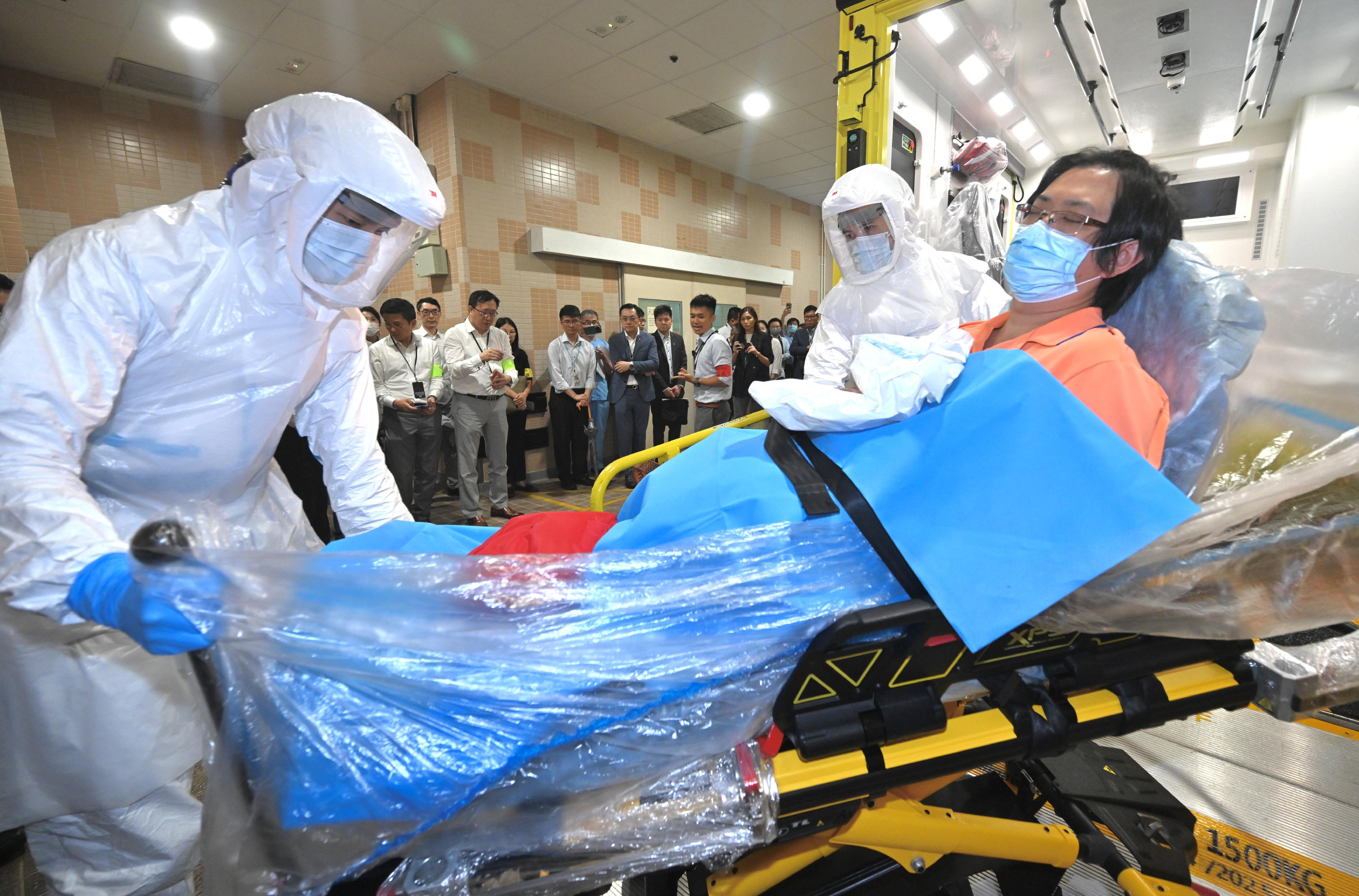 The Centre for Health Protection (CHP) of the Department of Health (DH) today (June 16) conducted a public health exercise codenamed "Charoite" in collaboration with various relevant government departments and organisations to strengthen stakeholders' response and co-ordination capabilities in handling suspected imported cases of Ebola disease and to enhance awareness among all units about the prevention and management of public health emergencies. Photo shows staff members of the Fire Services Department, in a simulated scenario, deploying their Infection Control and Critical Care Transfer Ambulance, which is equipped with a high-efficiency negative pressure system and specialised equipment, to transport a suspected Ebola patient to a designated hospital. Looking on are the Director of Health, Dr Ronald Lam, the Controller of the CHP of the DH, Dr Edwin Tsui, and other observers.
