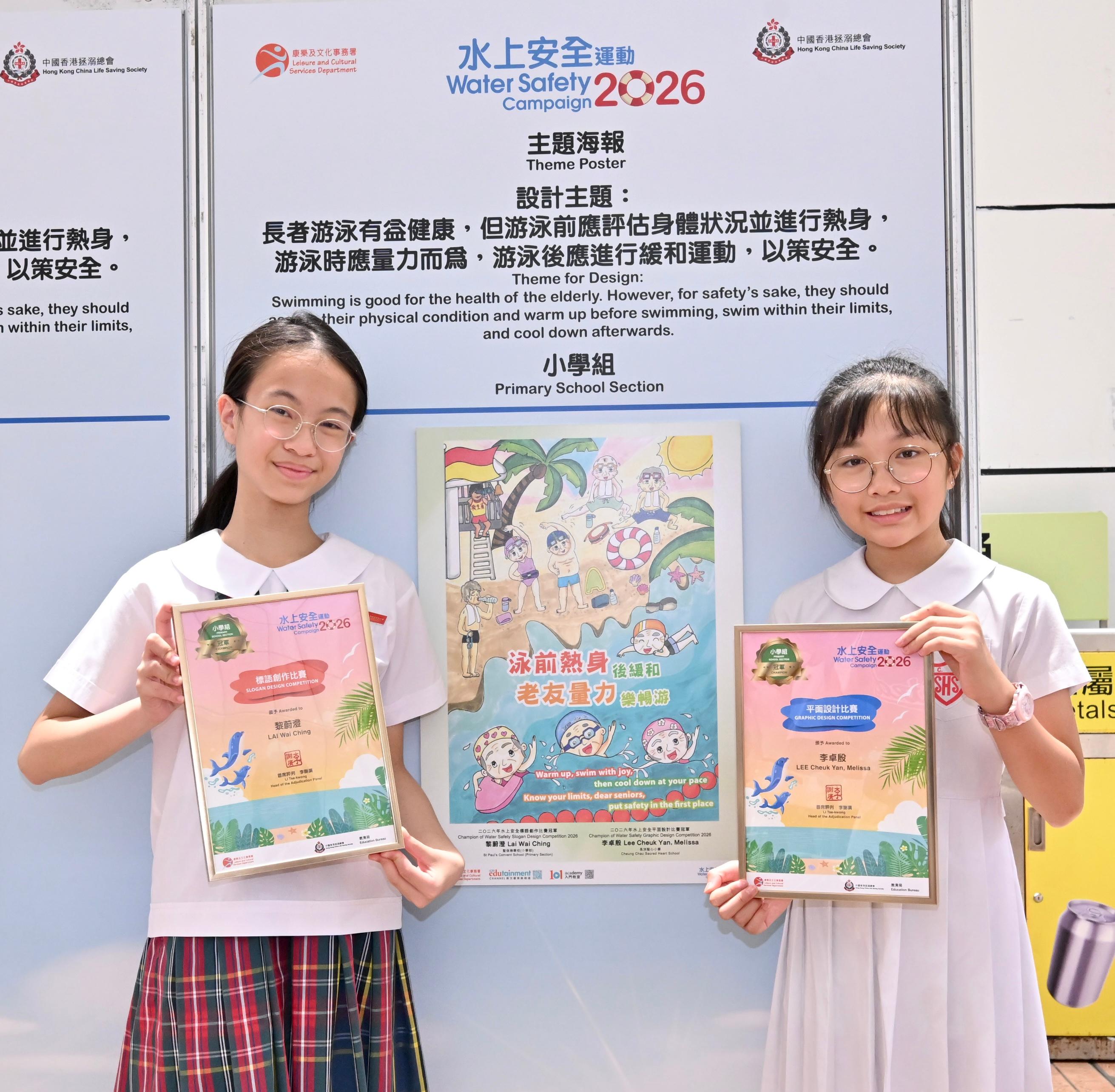 康樂及文化事務署與中國香港拯溺總會合辦的「二○二六年水上安全運動」標語創作和平面設計比賽今日（六月二十七日）舉行頒獎典禮。圖示奪得平面設計比賽小學組冠軍的李卓殷（右）及其得獎作品，以及憑「泳前熱身後緩和，老友量力樂暢游」奪得標語創作比賽小學組冠軍的黎蔚澄（左）。
