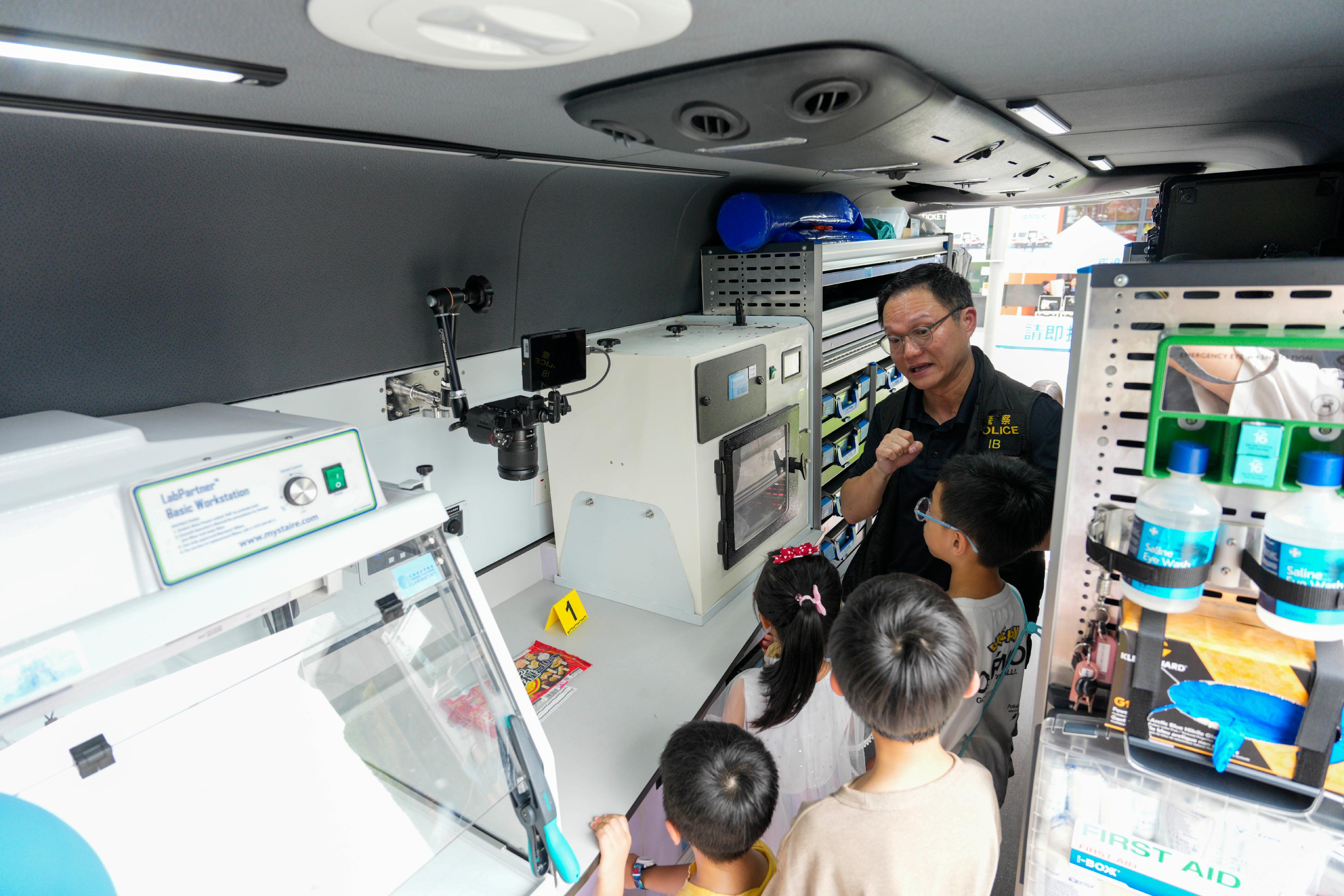 The Hong Kong Police Force today (June 28) held the Police Recruitment Day 2026 at the Kai Tak Youth Sports Ground. Photo shows an officer from the Identification Bureau introducing participants to various equipment inside the "CSI Mobile Laboratory", providing them a closer look at crime scene investigation techniques.
