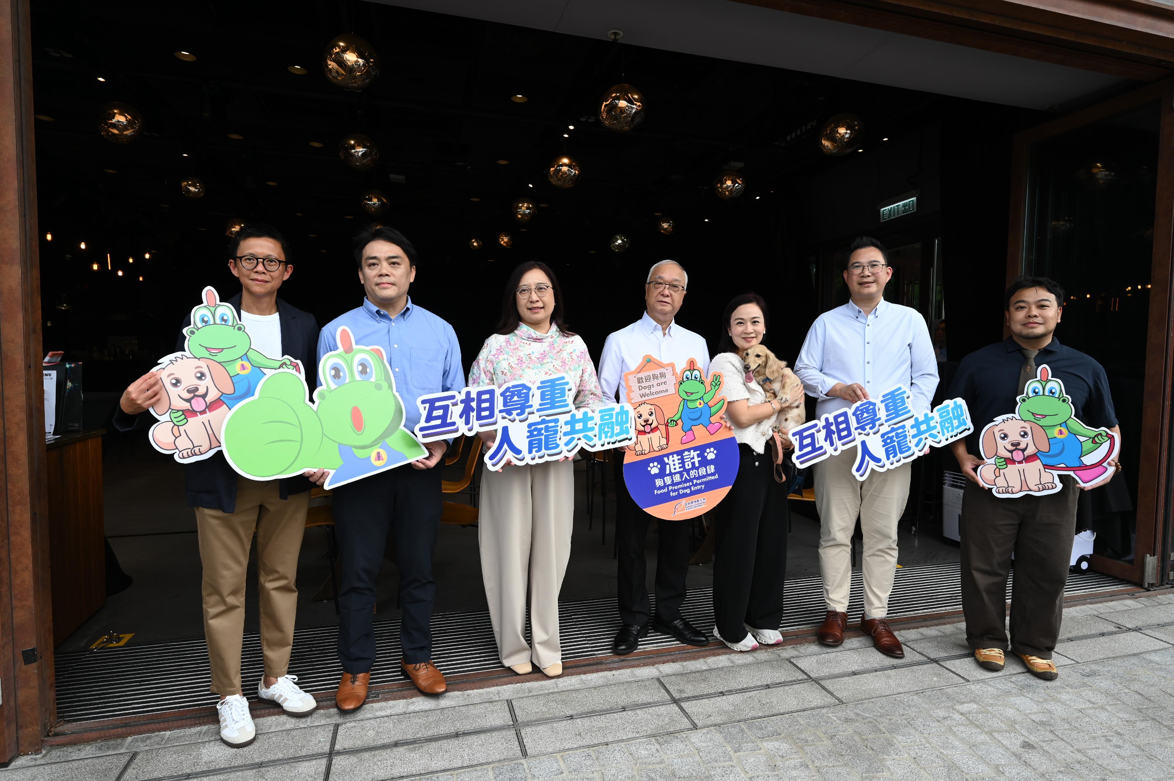 首批逾940間獲准食肆今日（七月九日）起可容許顧客攜帶狗隻進入。圖示環境及生態局局長謝展寰（中）、環境及生態局常任秘書長（食物）楊碧筠（左三）、食物環境衞生署署長袁旭健（左二），以及立法會食物安全及環境衞生事務委員會主席陳凱欣（右三）和副主席楊永杰（右二）下午到訪西九文化區一所獲准食肆，了解新措施實施首日的情況，並與食肆經營者（右一）合照。